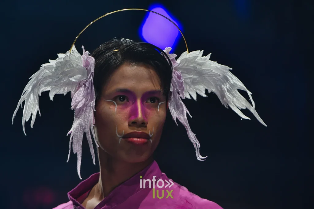 Portrait : coiffe d’ailes blanches et auréole dorée, chemise fuchsia, maquillage rose — Alimac, « Mystic Blossom », Lux Fashion Week 2026, Arlon
