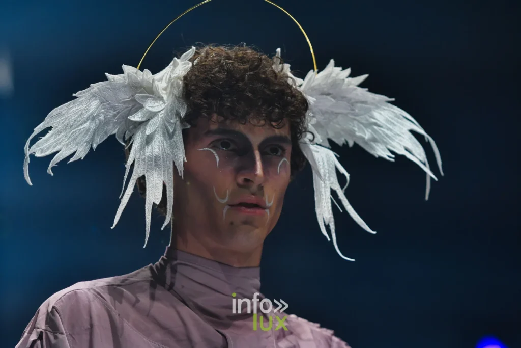 Portrait : coiffe d’ailes blanches, col montant mauve, maquillage graphique — Alimac, « Mystic Blossom », Lux Fashion Week 2026, Arlon