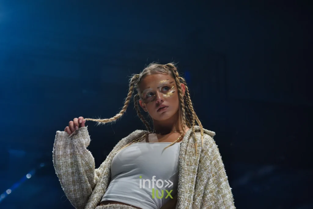 Veste en lainage texturé beige sur un débardeur blanc, tresses et maquillage pailleté — Violette Briel, « L’Héritage », Lux Fashion Week 2026, Arlon