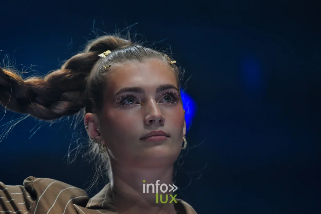 Portrait : longue tresse relevée, maquillage pailleté, veste brune à rayures — Violette Briel, « L’Héritage », Lux Fashion Week 2026, Arlon