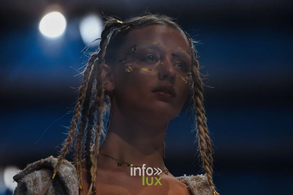 Portrait : tresses et paillettes dorées sur le visage, veste en lainage texturé — Violette Briel, « L’Héritage », Lux Fashion Week 2026, Arlon