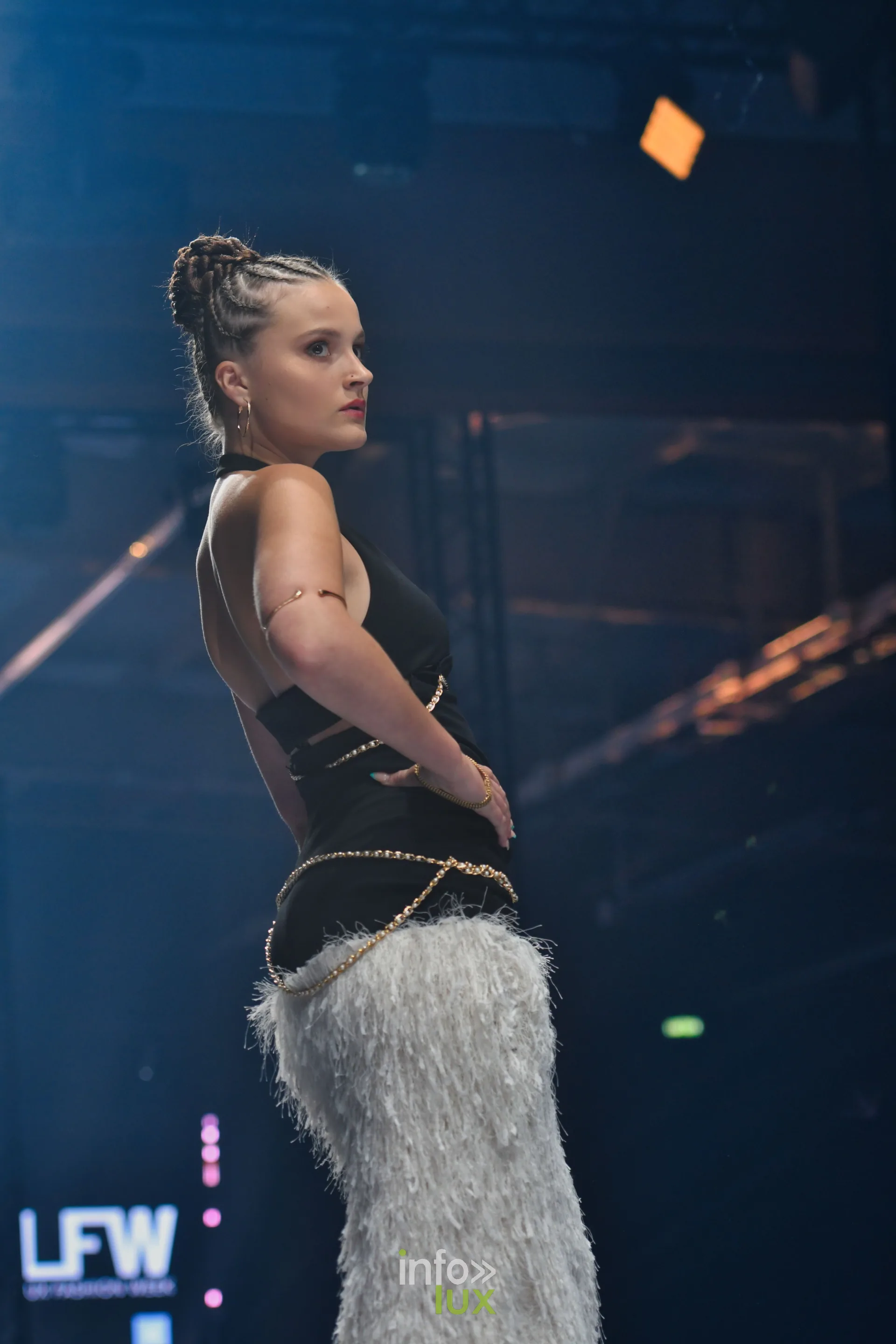 Haut noir dos nu, chaînes dorées et jupe à franges grises, de profil, collection « Le Fil Sacré » de Christelle Bukasa, Lux Fashion Week 2026, Arlon