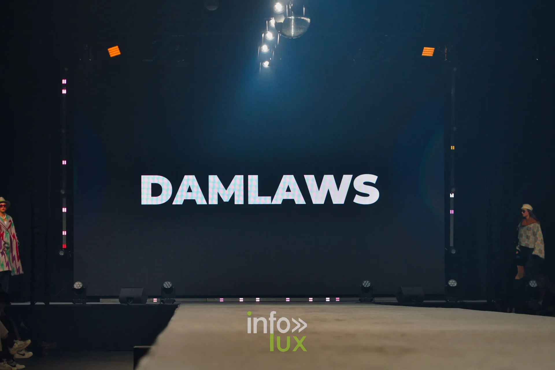 L’écran de scène affiche « DAMLAWS » au-dessus du podium, juste avant le passage — Damlaws, « The Dam Star », Lux Fashion Week 2026, Arlon