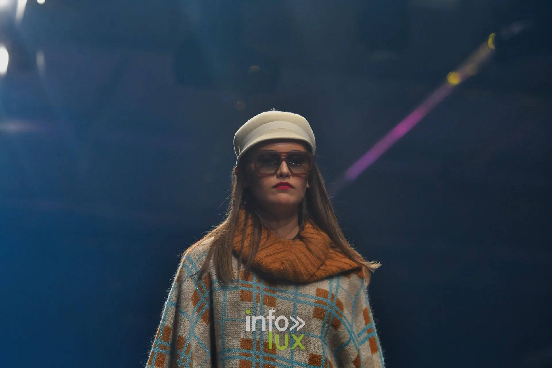 Poncho à carreaux beige, bleu ciel et orange, grosse écharpe orange, casquette blanche — Damlaws, « The Dam Star », Lux Fashion Week 2026, Arlon
