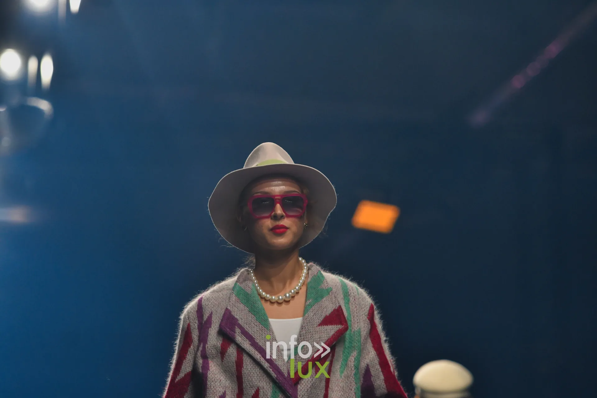 Manteau en maille gris à motifs d’éclairs rouges, violets et verts, chapeau blanc et lunettes roses — Damlaws, « The Dam Star », Lux Fashion Week 2026, Arlon