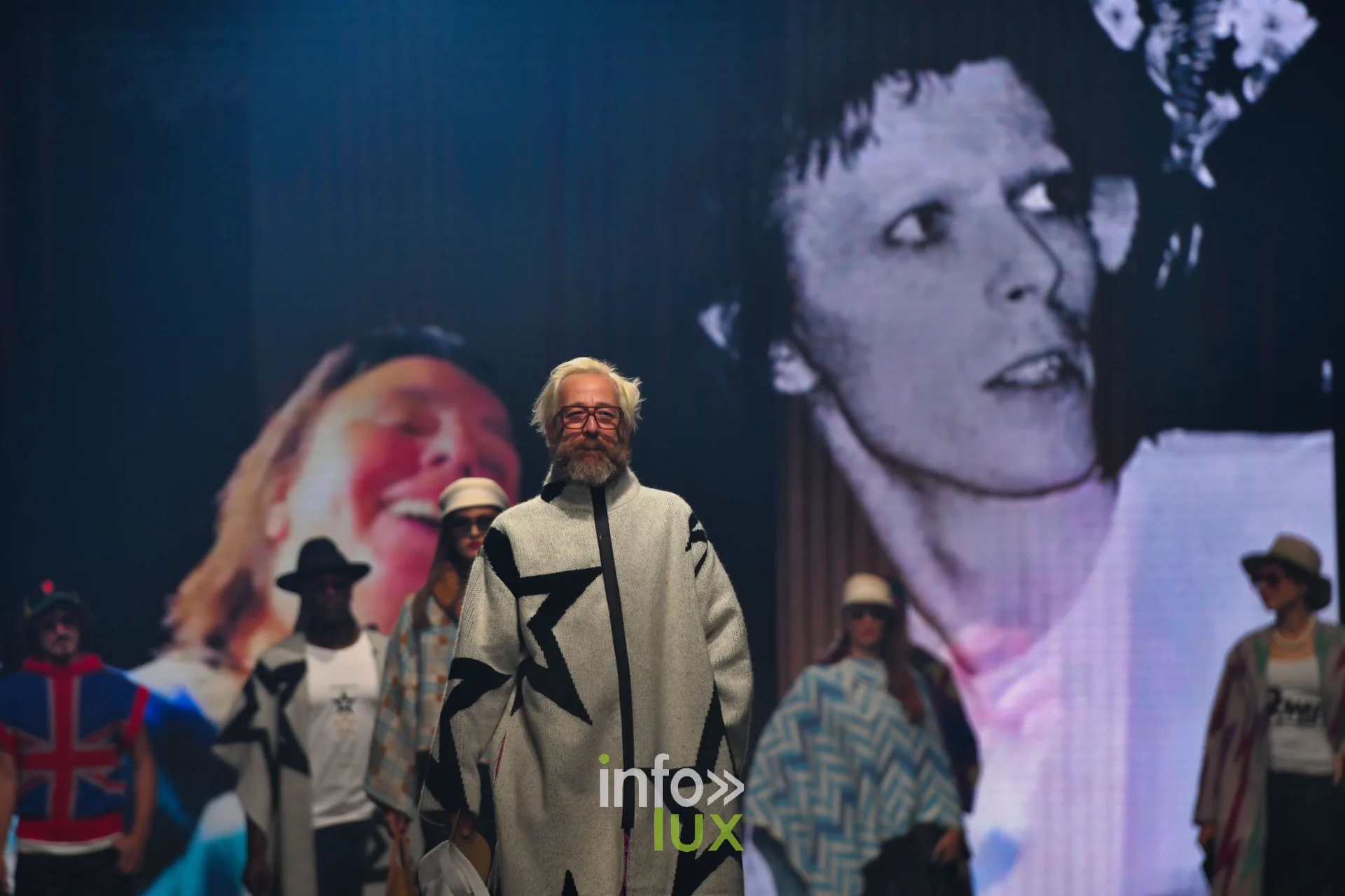 Le groupe au bout du podium devant un portrait en noir et blanc projeté ; manteau gris à étoiles noires au premier plan — Damlaws, « The Dam Star », Lux Fashion Week 2026, Arlon