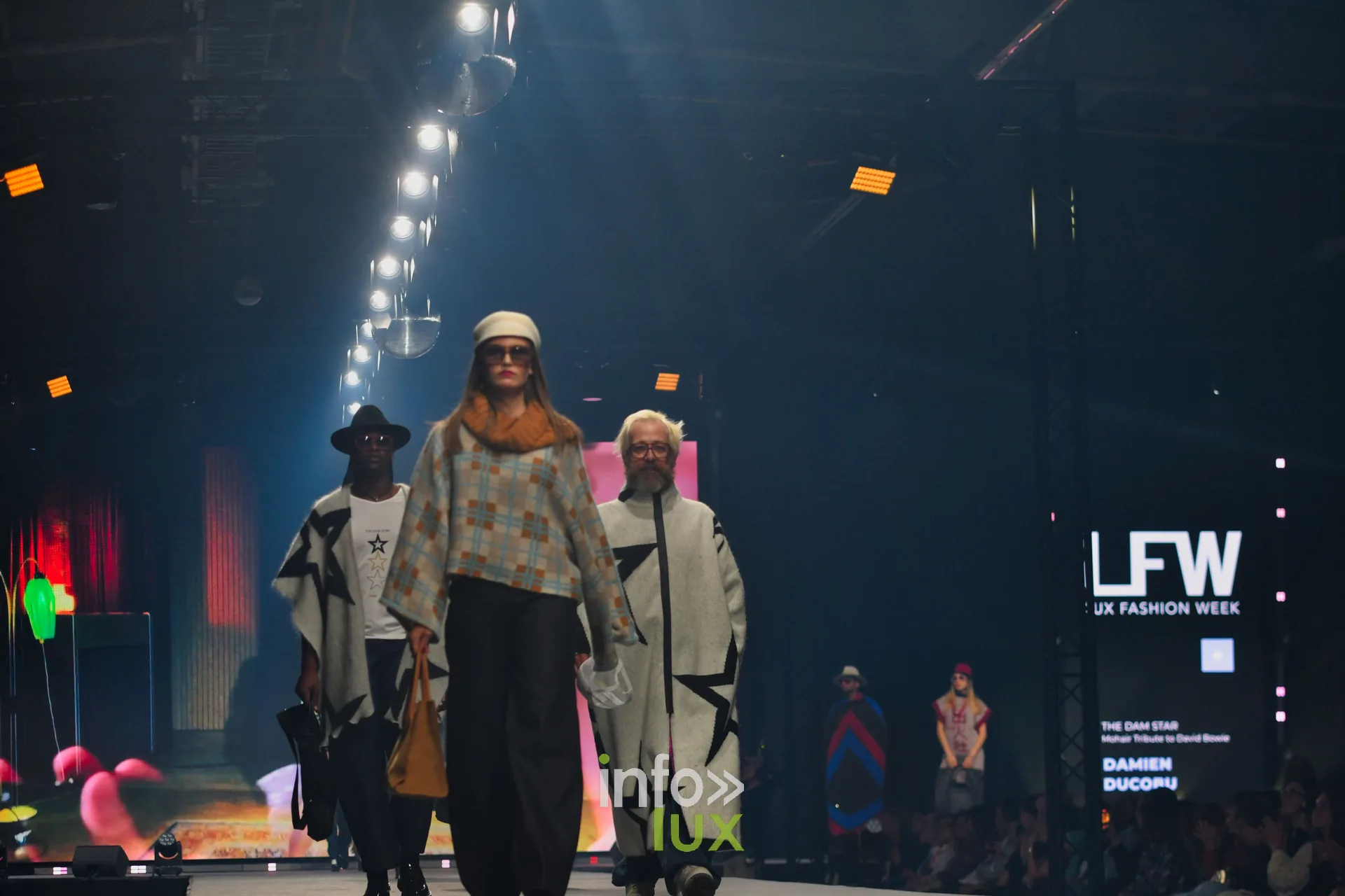 Trois silhouettes avancent sur le podium ; l’écran latéral LFW affiche le nom de la collection — Damlaws, « The Dam Star », Lux Fashion Week 2026, Arlon