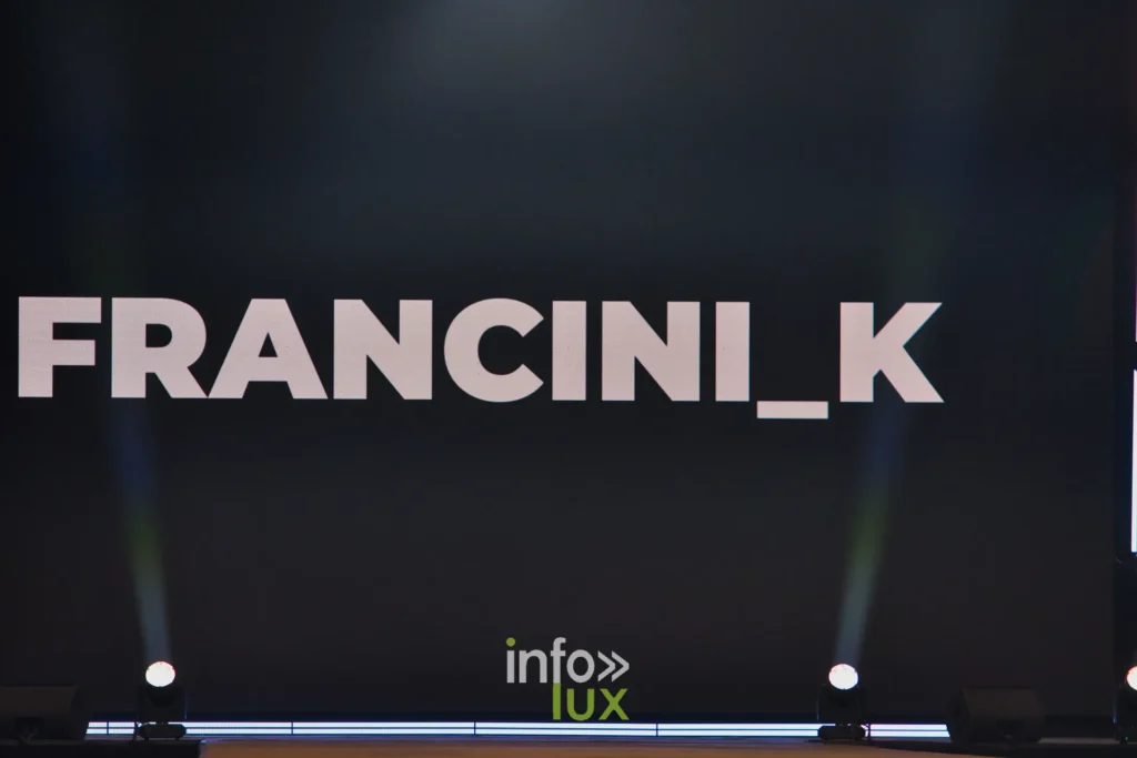 Le nom FRANCINI_K affiché sur l’écran de scène avant le passage — Francini_K, « La géométrie des fleurs », Lux Fashion Week 2026, Arlon