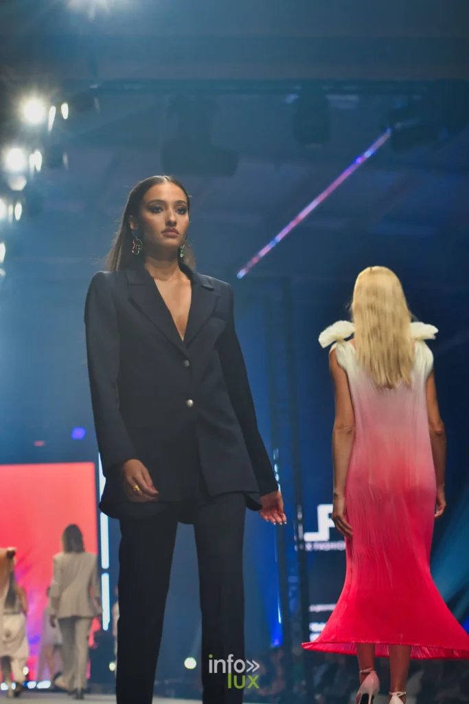 Tailleur-pantalon bleu marine et, de dos, la robe plissée en dégradé blanc-fuchsia — Francini_K, « La géométrie des fleurs », Lux Fashion Week 2026, Arlon