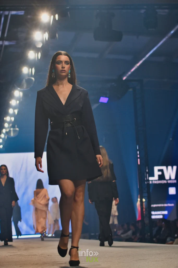 Robe-manteau noire croisée et ceinturée, portée avec des escarpins noirs — Francini_K, « La géométrie des fleurs », Lux Fashion Week 2026, Arlon