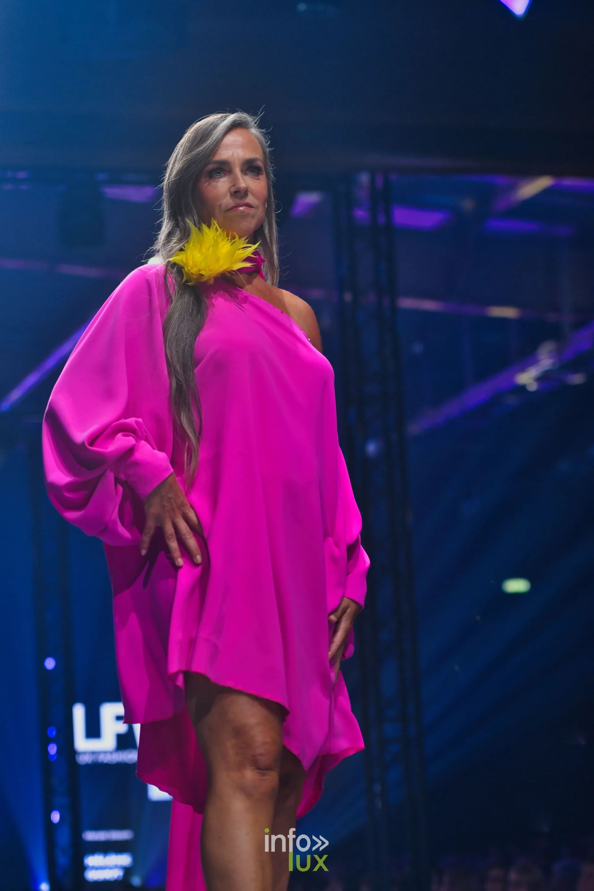 Robe fuchsia asymétrique à une épaule et manche ample, fleur de plumes jaunes, collection « Meraki bloom » d’Hélène Guiot, Lux Fashion Week 2026, Arlon