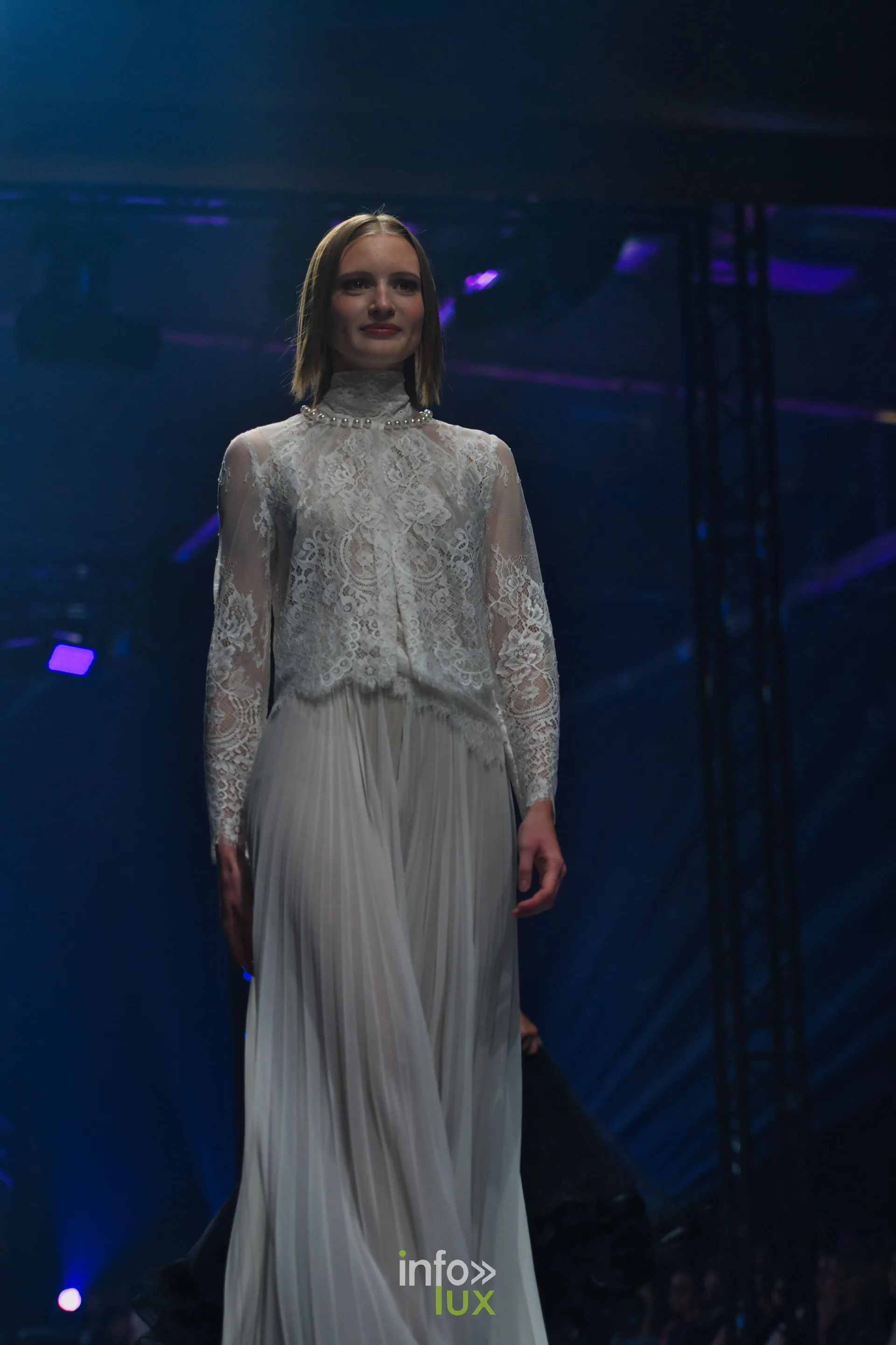Blouse en dentelle blanche à col montant et jupe longue plissée blanche, collection « Meraki bloom » d’Hélène Guiot, Lux Fashion Week 2026, Arlon