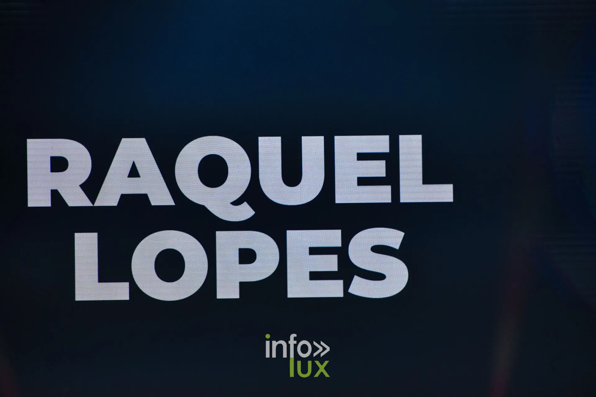 L’écran de scène affiche « RAQUEL LOPES » juste avant le passage — R. Lopes, « Raízes d’Ouro », Lux Fashion Week 2026, Arlon