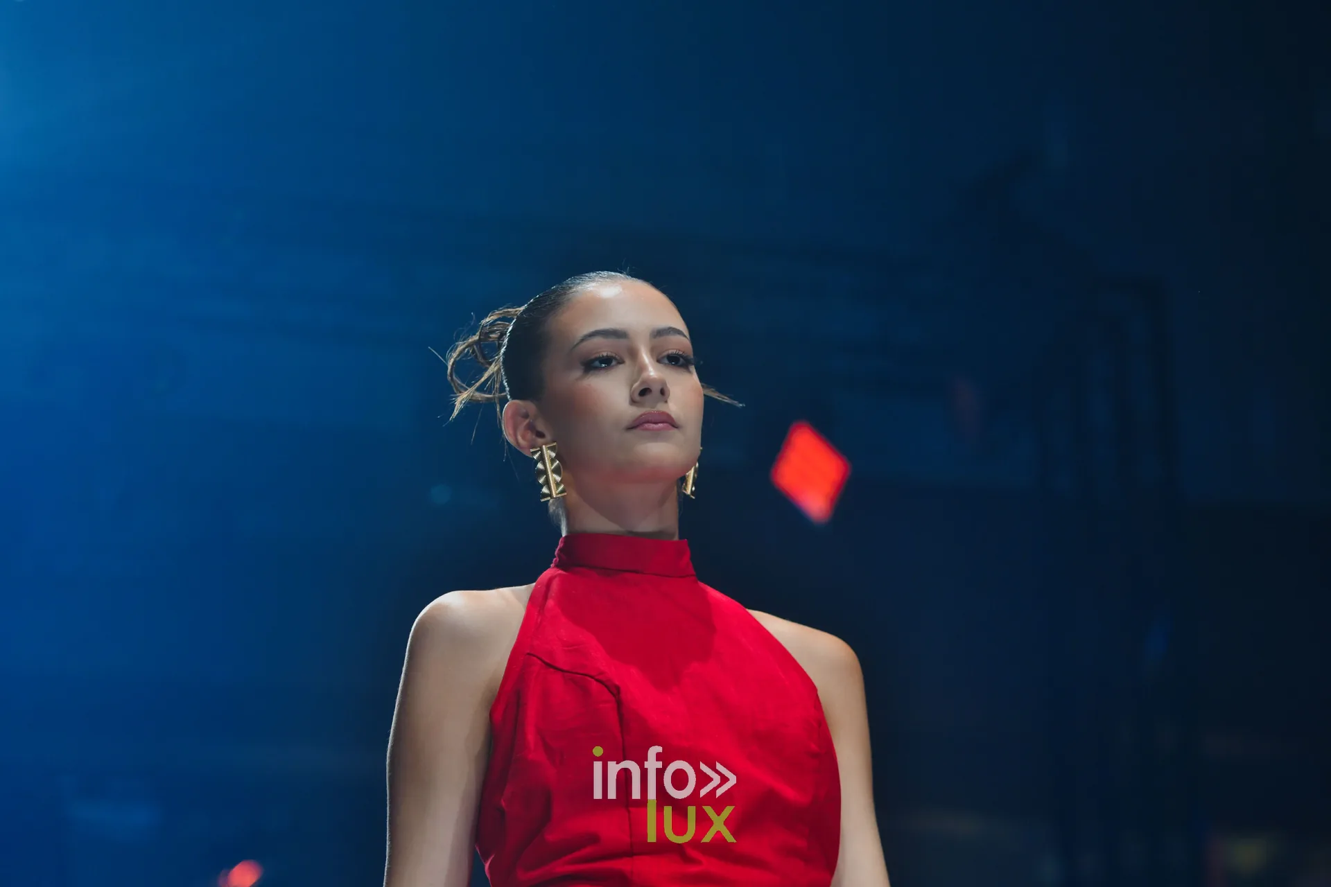 Robe rouge à col montant et dos nu, boucles d’oreilles dorées — R. Lopes, « Raízes d’Ouro », Lux Fashion Week 2026, Arlon