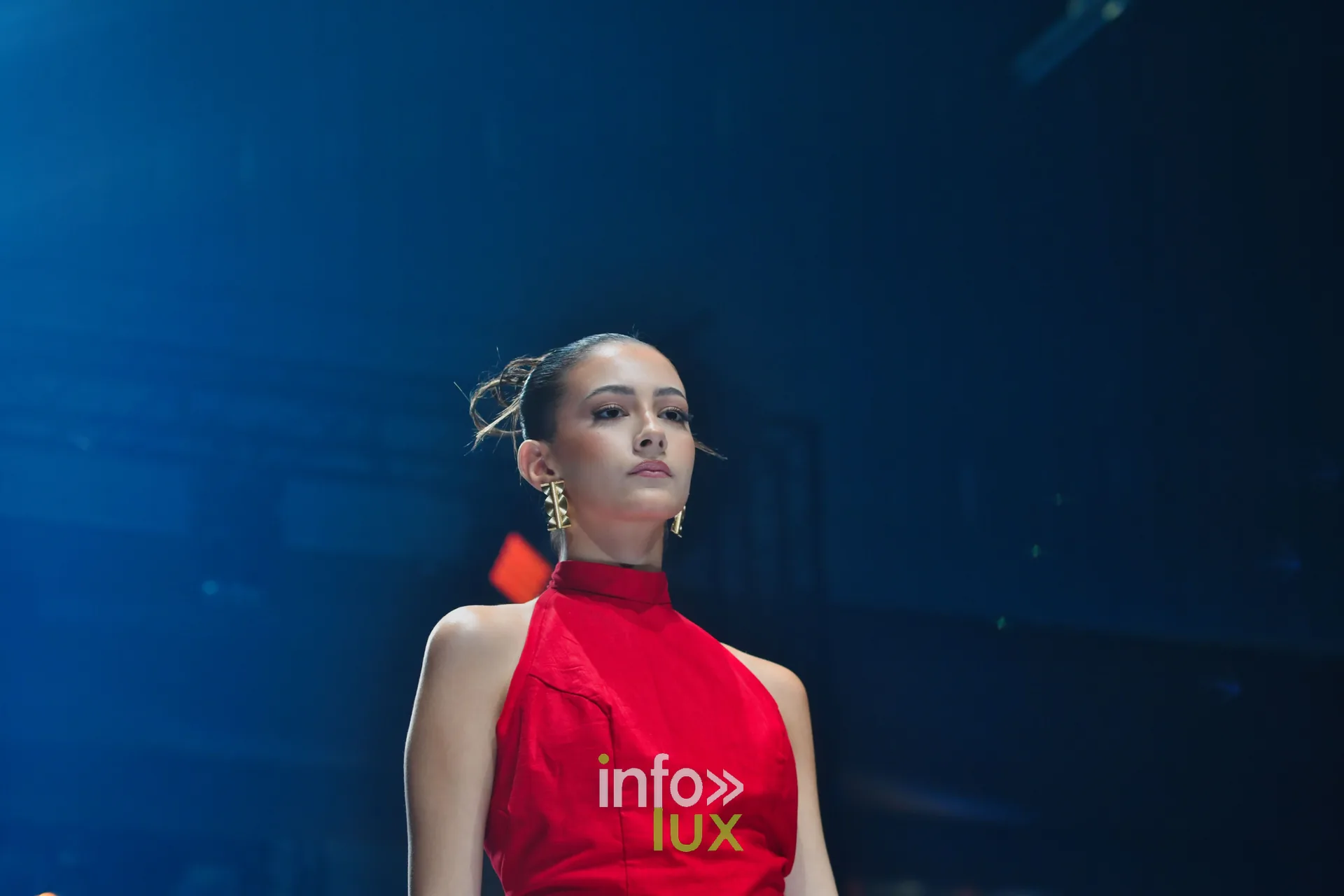 Robe rouge à col montant et dos nu, cheveux relevés — R. Lopes, « Raízes d’Ouro », Lux Fashion Week 2026, Arlon