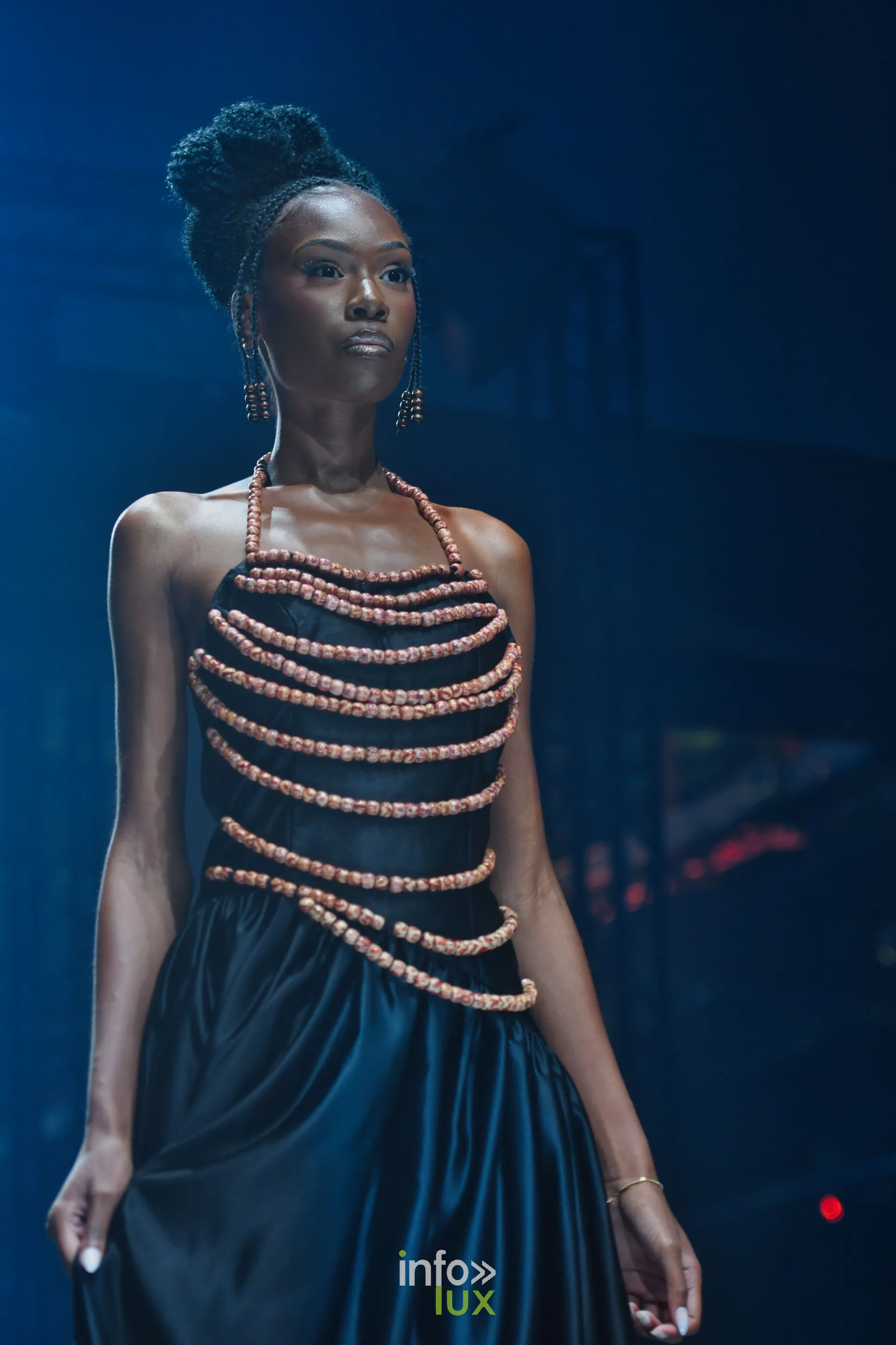 Haut en rangs de perles orangées sur robe longue en satin noir — R. Lopes, « Raízes d’Ouro », Lux Fashion Week 2026, Arlon
