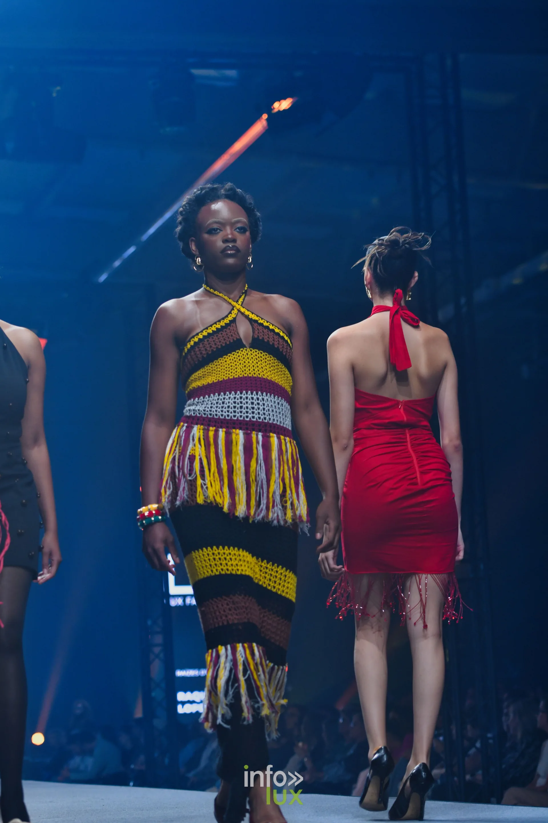 Robe longue en crochet rayé jaune, noir et rouge à franges ; à droite, robe rouge dos nu à franges — R. Lopes, « Raízes d’Ouro », Lux Fashion Week 2026, Arlon