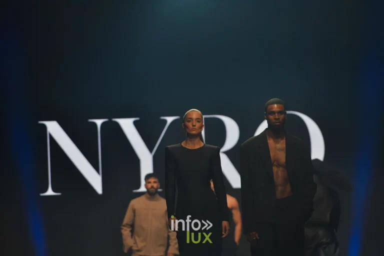 Robe longue noire et costume noir porté torse nu, devant l’écran « NYRO », collection « NYRO » de Mathieu Panzokou, Lux Fashion Week 2026, Arlon