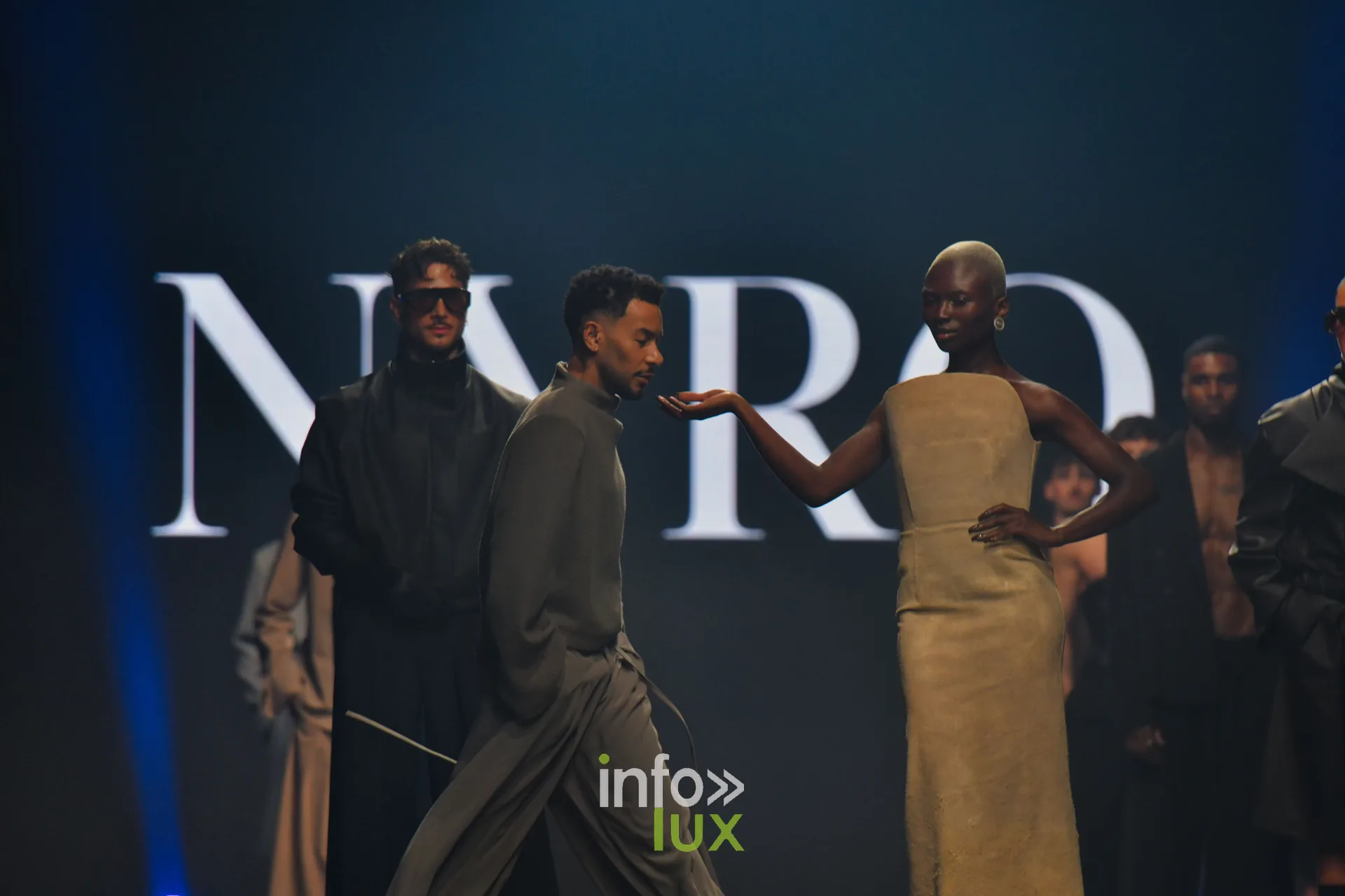 Ensemble ample gris-vert et robe bustier beige, devant l’écran « NYRO », collection « NYRO » de Mathieu Panzokou, Lux Fashion Week 2026, Arlon