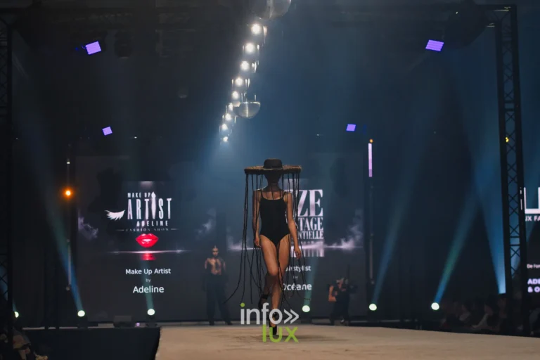 Léa Denis, ballerine en pointes et justaucorps noir, sous un chapeau en cheveux tressés, sur le podium devant les écrans Make Up Artist Adeline et OZE Backstage, Lux Fashion Week 2026, Arlon