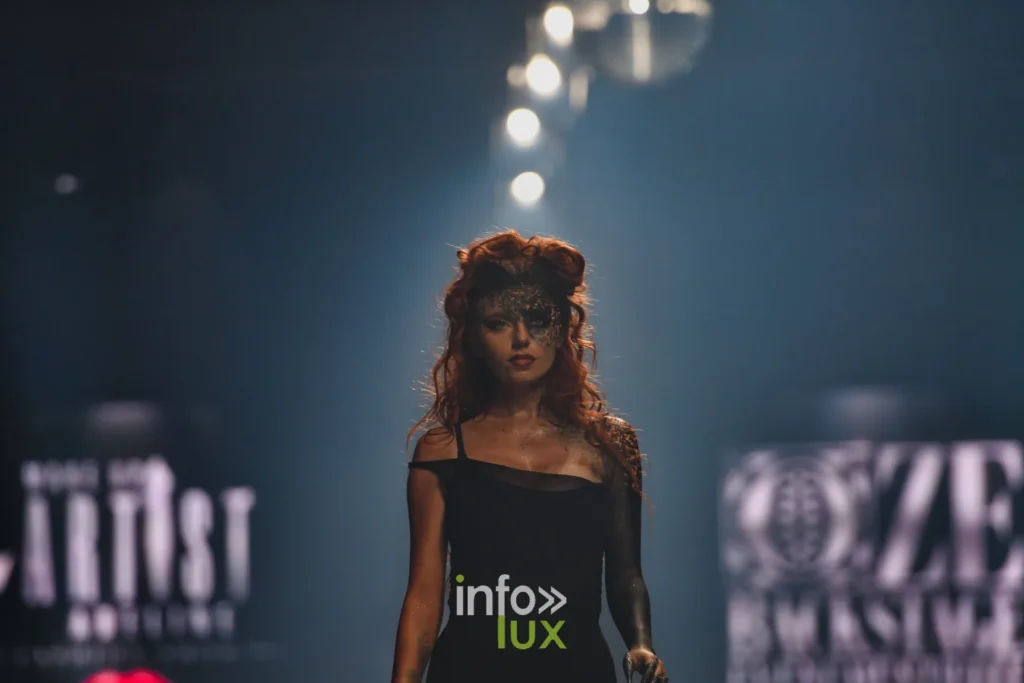 Mannequin à la coiffure rousse volumineuse et au masque pailleté, devant les écrans Artist Adeline et OZE Backstage, Lux Fashion Week 2026, Arlon