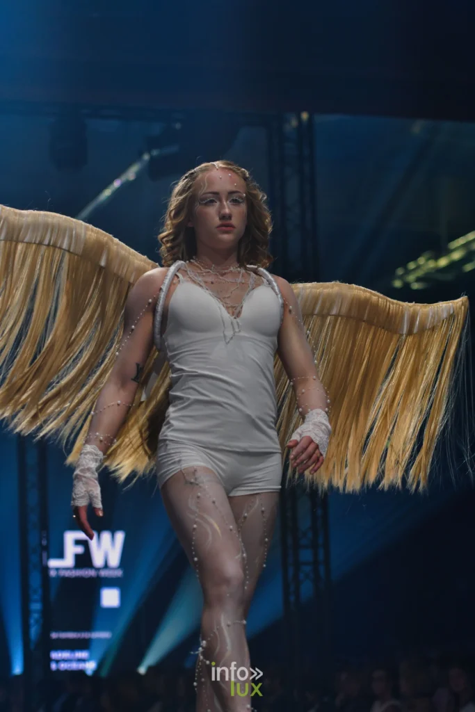 Nova en body blanc, perles et ailes dorées à franges, au milieu du podium, Lux Fashion Week 2026, Arlon