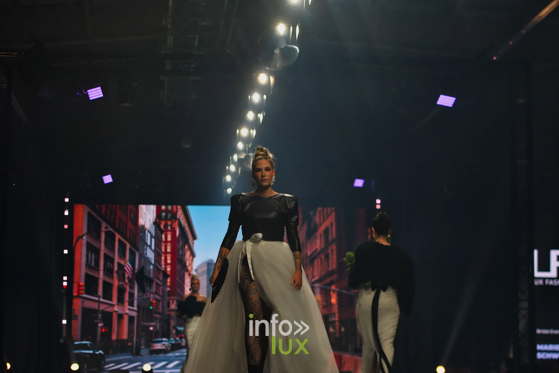 Haut noir à manches bouffantes et jupe longue en tulle blanc ouverte sur un collant en dentelle, devant le décor new-yorkais, collection « Bridal Everyday » de Marie Schweisthal, Lux Fashion Week 2026, Arlon