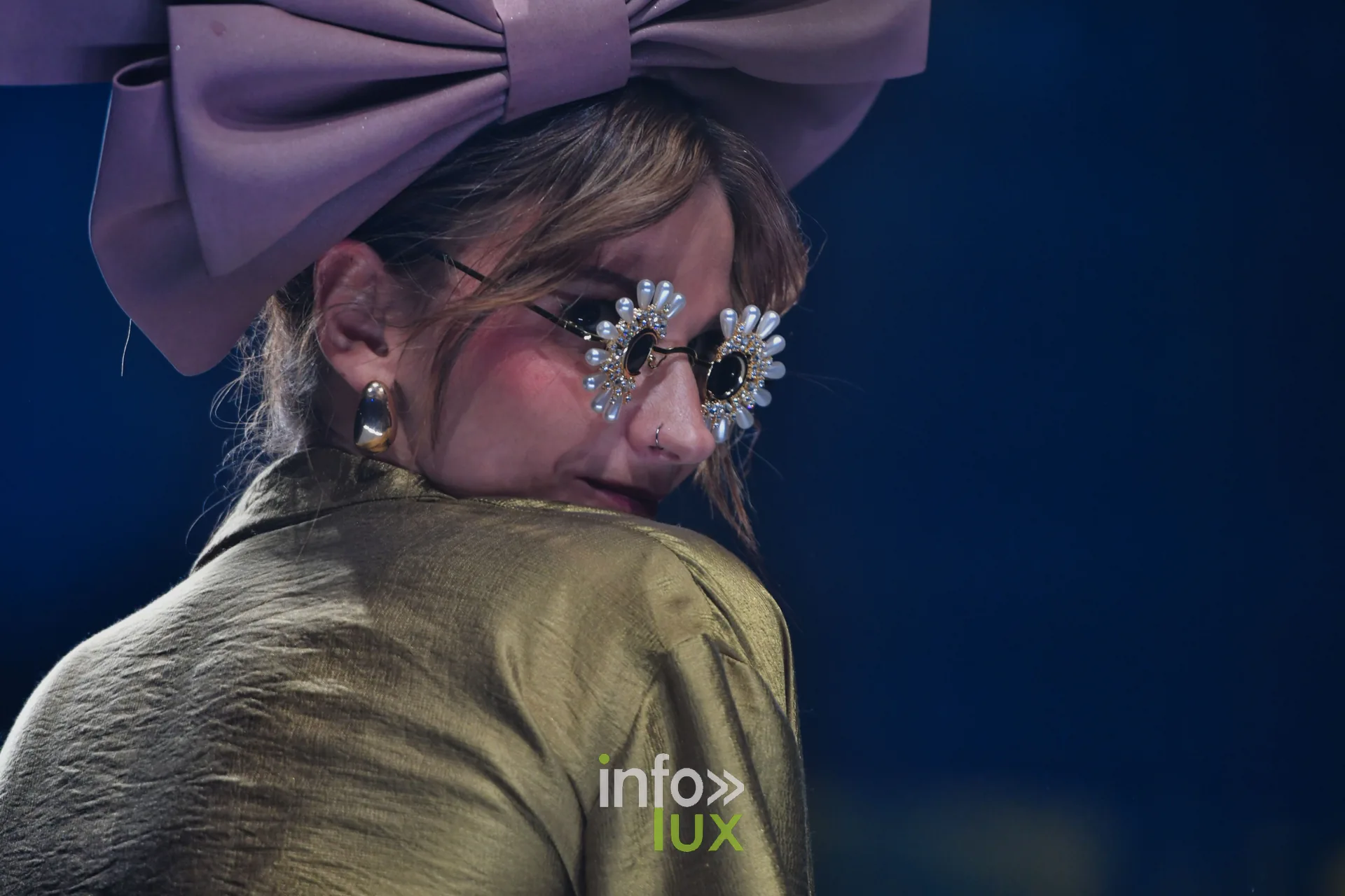 Nœud mauve géant, lunettes ornées de fleurs et veste dorée satinée — Charlotte Spoidenne, « Diffraction », Lux Fashion Week 2026, Arlon