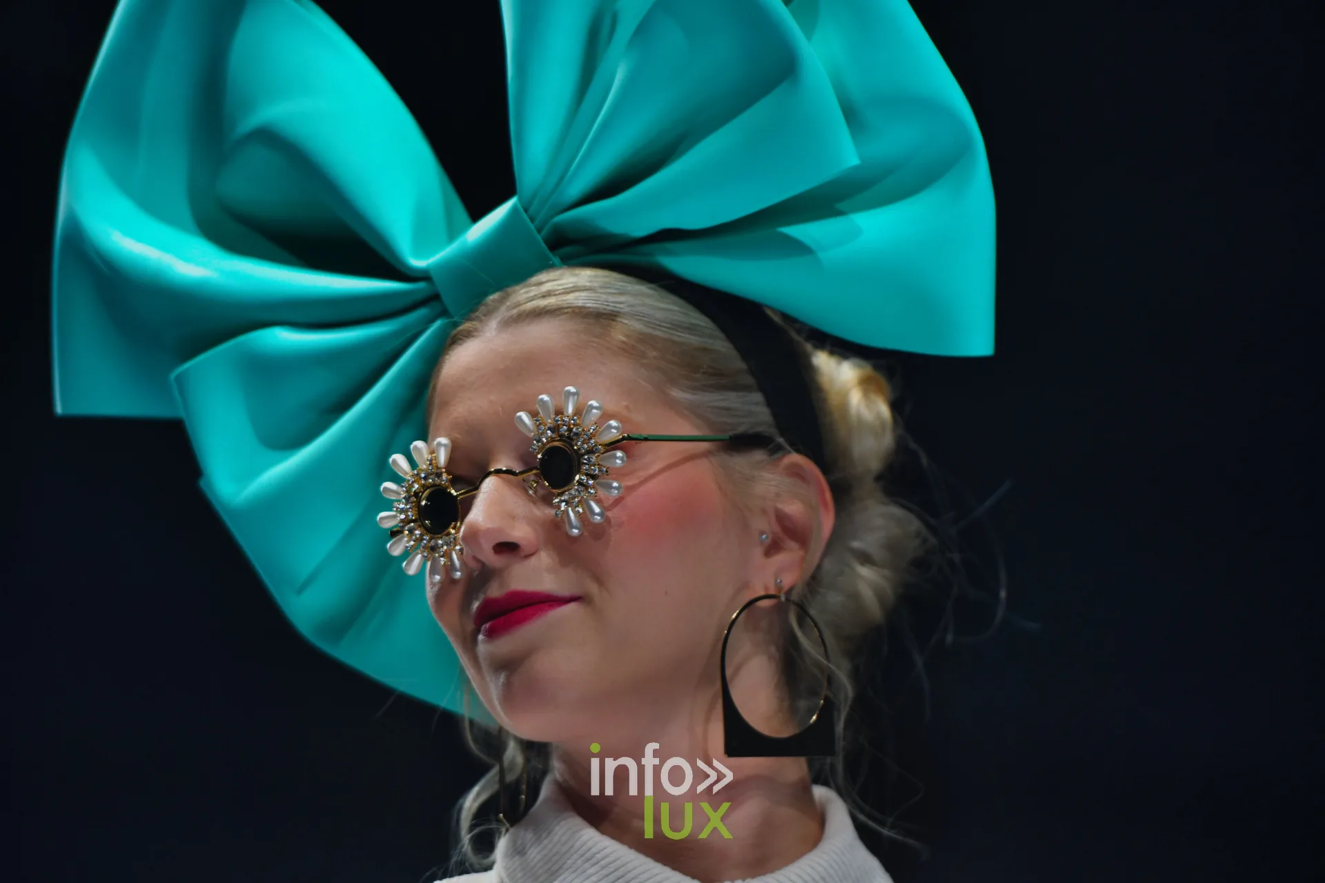 Nœud turquoise géant et lunettes ornées de fleurs, en gros plan — Charlotte Spoidenne, « Diffraction », Lux Fashion Week 2026, Arlon