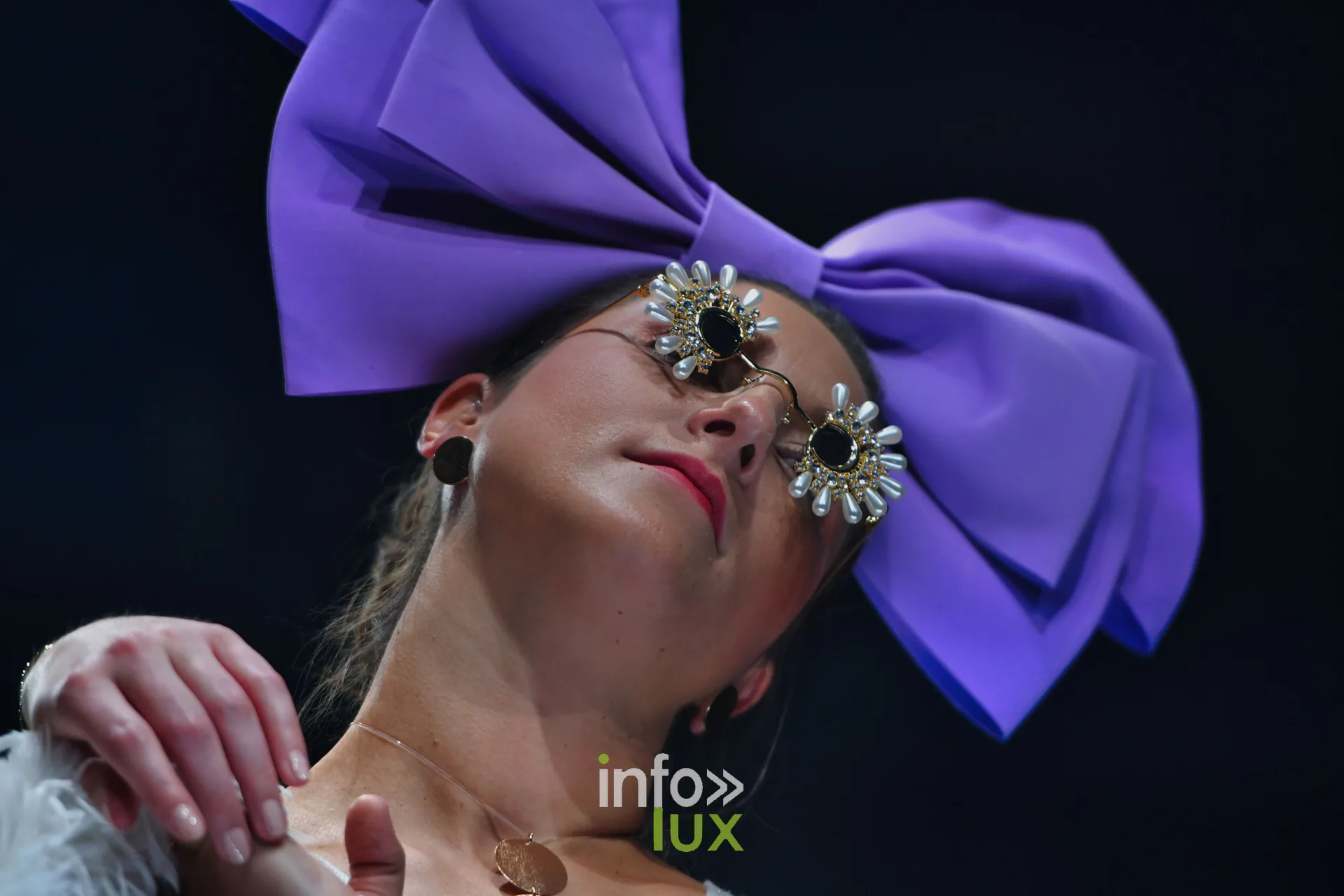 Nœud violet géant et plumes blanches, tête inclinée — Charlotte Spoidenne, « Diffraction », Lux Fashion Week 2026, Arlon