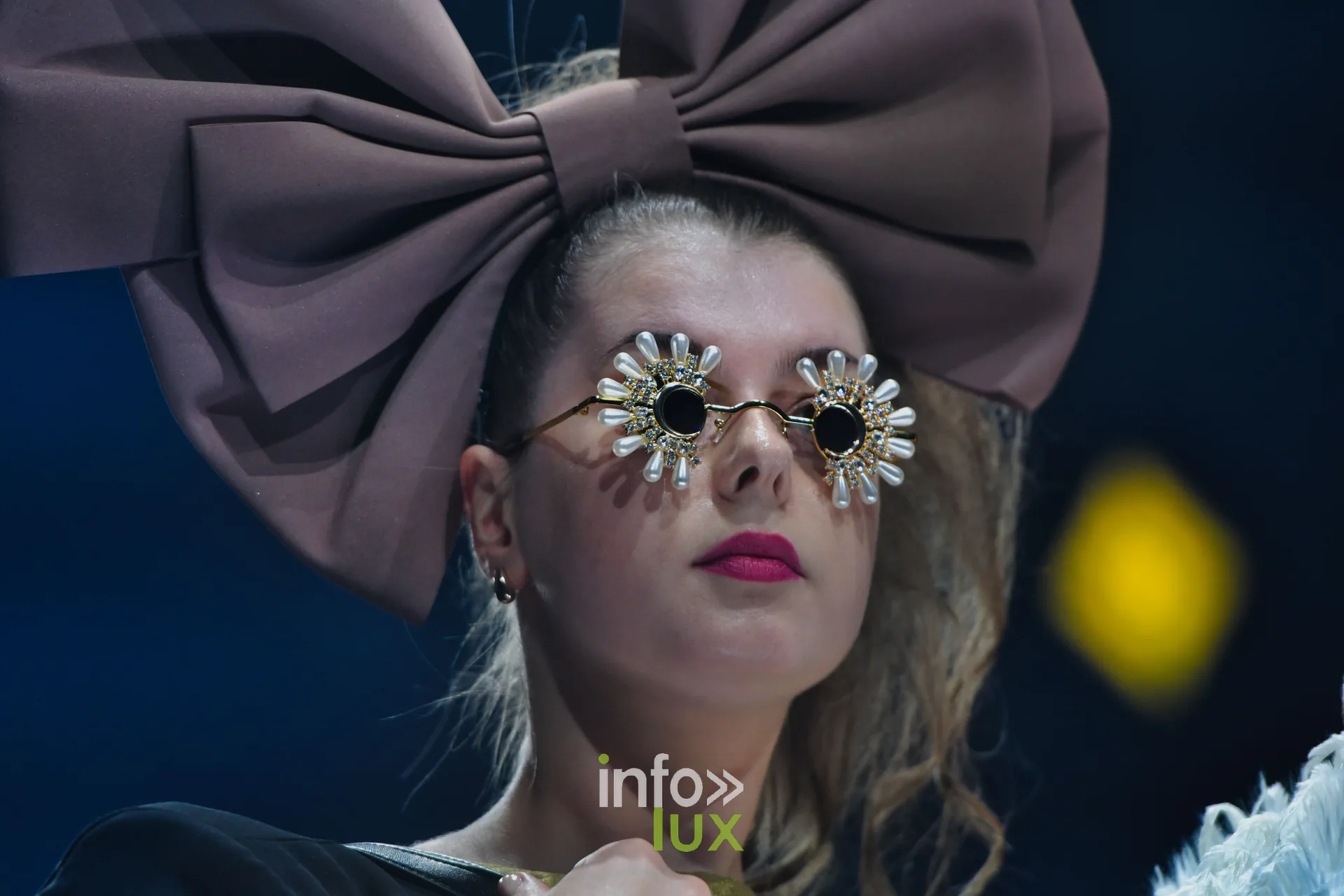 Nœud géant taupe et lunettes ornées de fleurs, en gros plan — Charlotte Spoidenne, « Diffraction », Lux Fashion Week 2026, Arlon