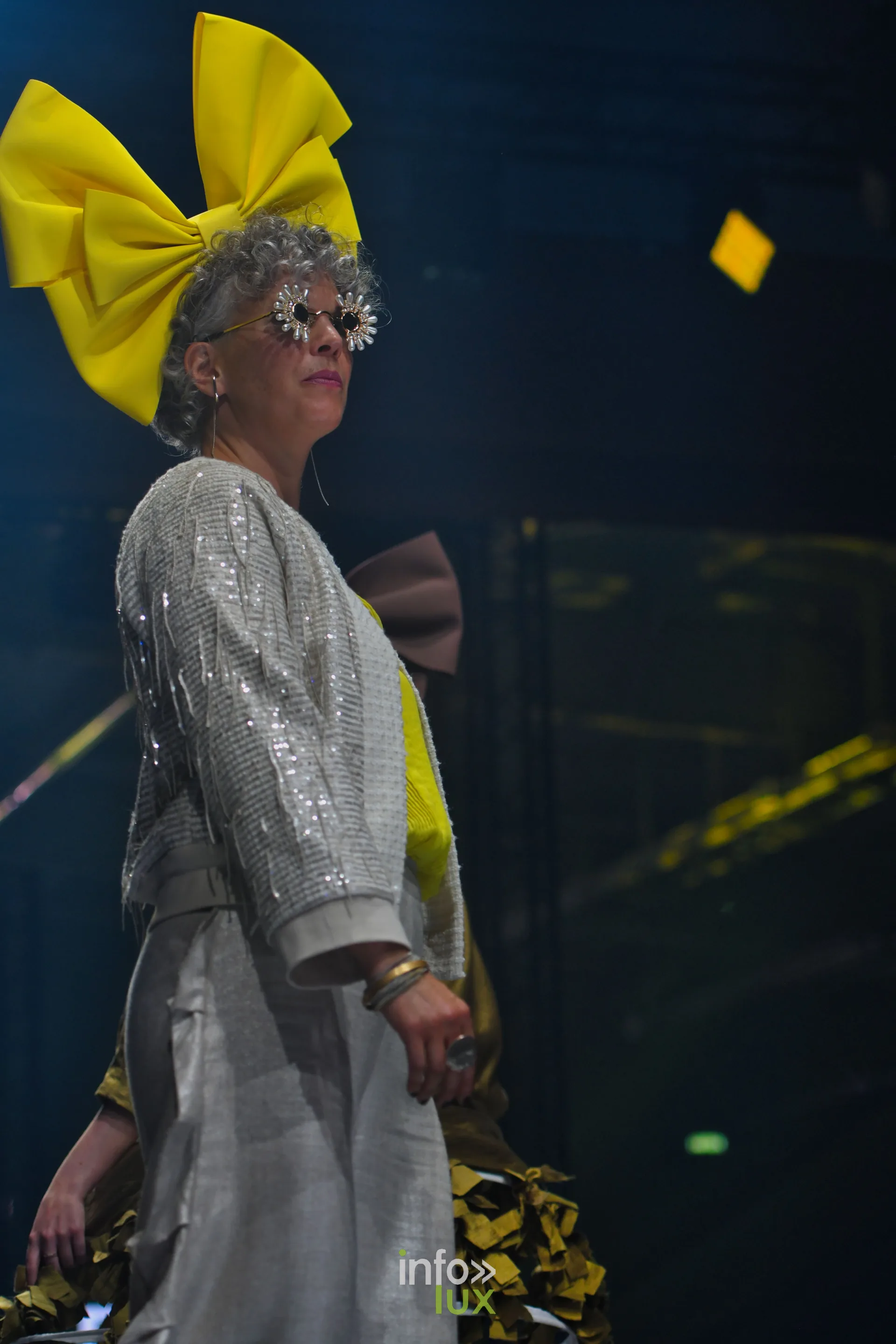 Nœud jaune géant, veste argentée à sequins et pantalon large gris — Charlotte Spoidenne, « Diffraction », Lux Fashion Week 2026, Arlon