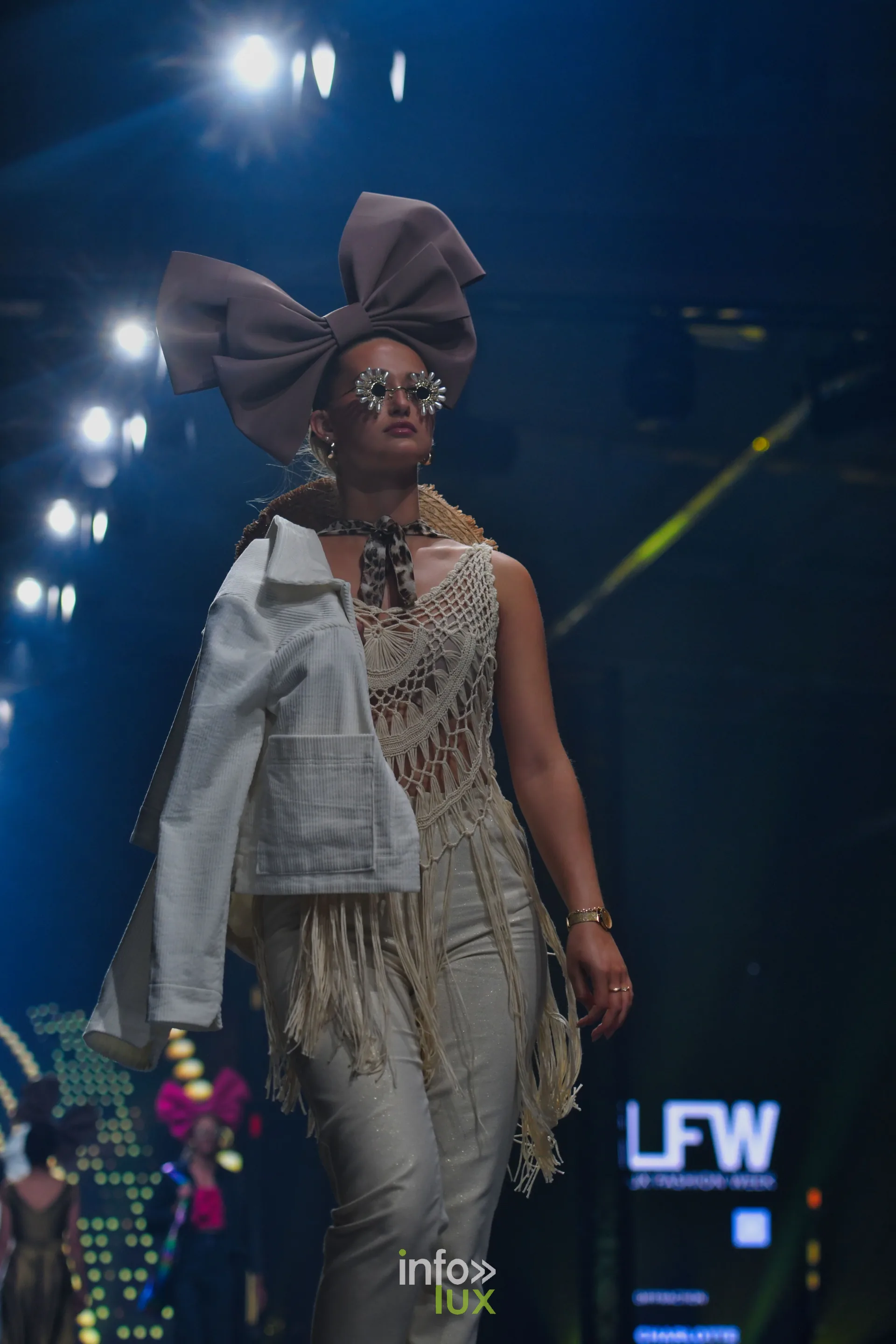 Ensemble en crochet écru à franges et veste blanche portée sur l’épaule, en pied — Charlotte Spoidenne, « Diffraction », Lux Fashion Week 2026, Arlon