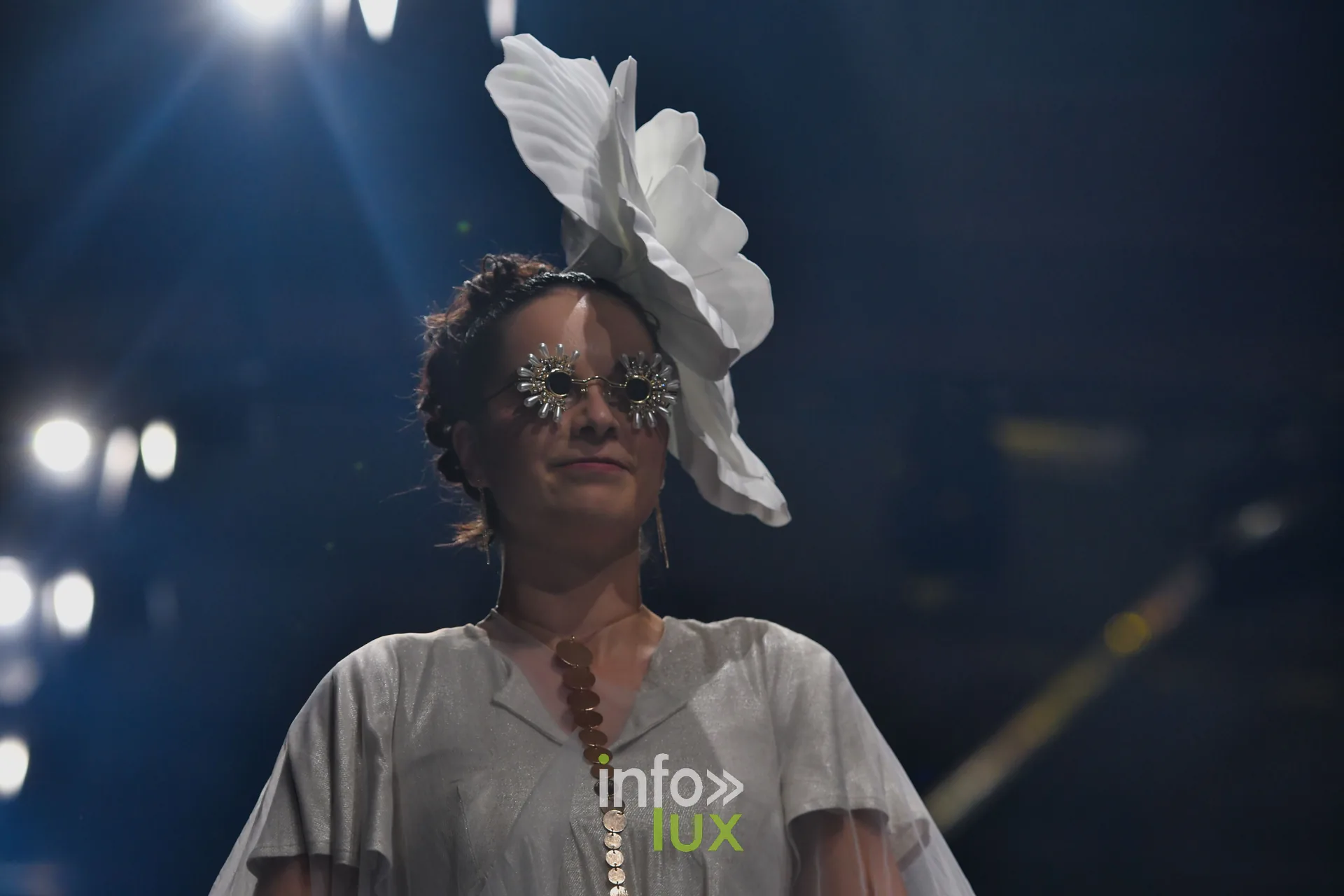 Robe grise fluide à boutons dorés et grande fleur blanche en coiffe — Charlotte Spoidenne, « Diffraction », Lux Fashion Week 2026, Arlon