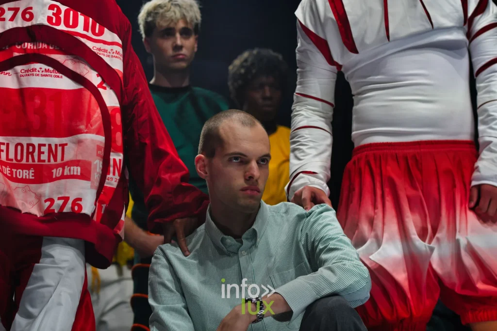 Salut final : short bouffant en dégradé rouge et blanc, dossard imprimé « FLORENT » et « 10 km » — Florent Stevens, « S’print », Lux Fashion Week 2026, Arlon