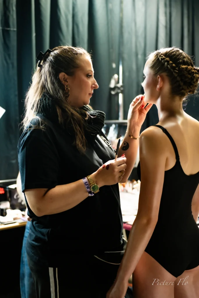 Léa Denis, en justaucorps noir, au maquillage dans les coulisses du show « Les talents de l’ombre », Lux Fashion Week 2026, Arlon