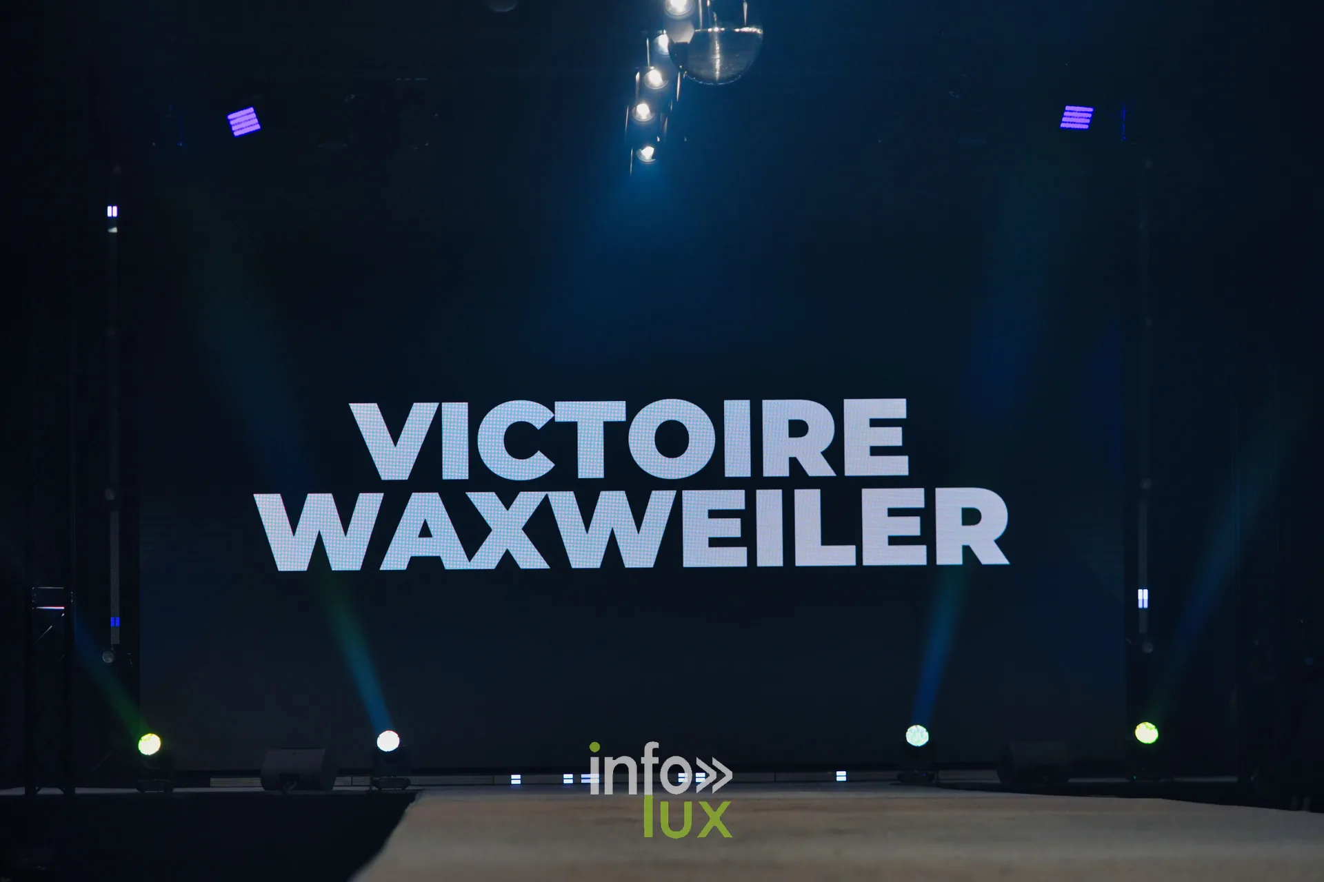 L’écran de scène affiche « VICTOIRE WAXWEILER » juste avant le passage — Victoire Waxweiler, « Fragments », Lux Fashion Week 2026, Arlon