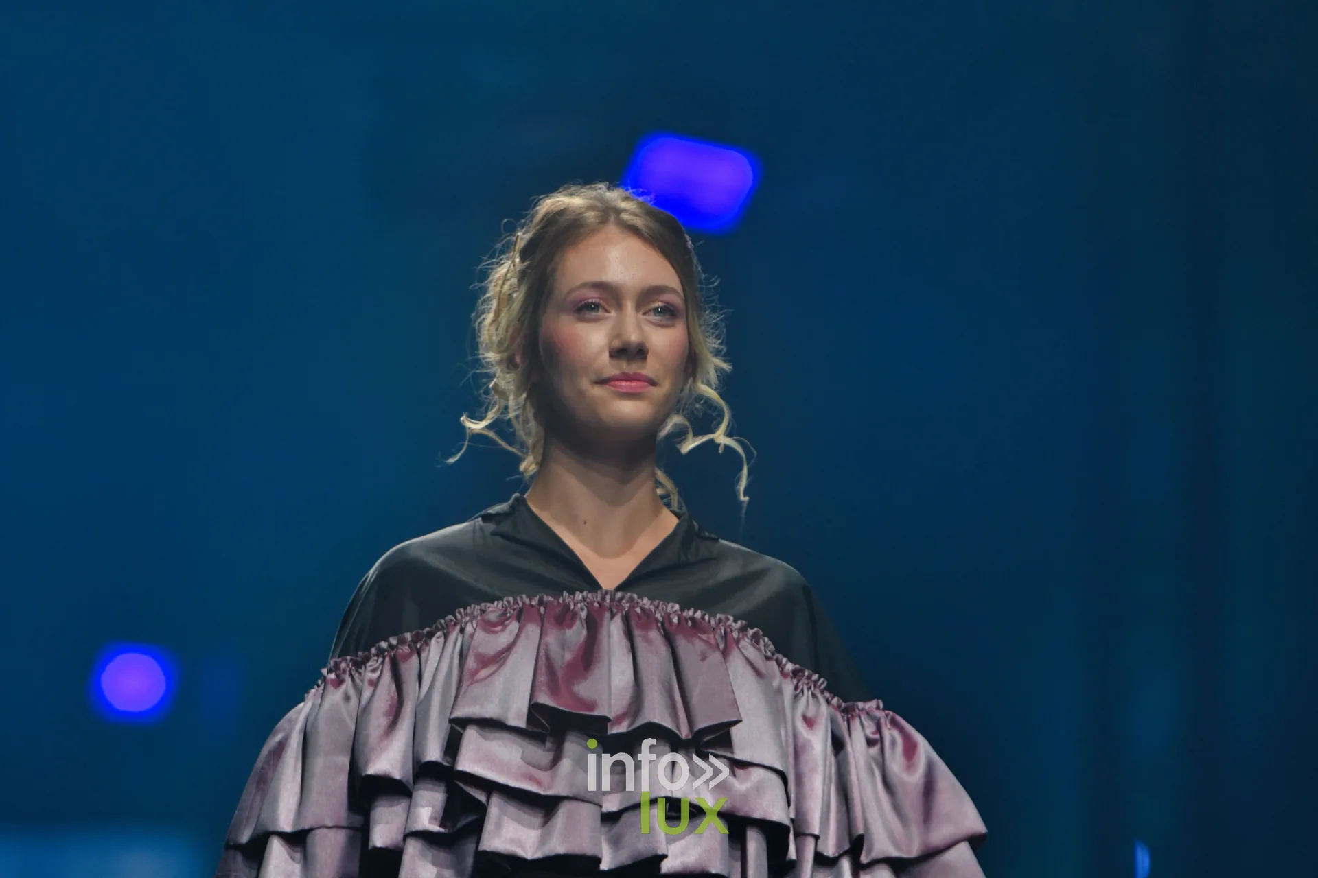 Cape en satin vieux rose à volants étagés sur blouse noire à col en V — Victoire Waxweiler, « Fragments », Lux Fashion Week 2026, Arlon