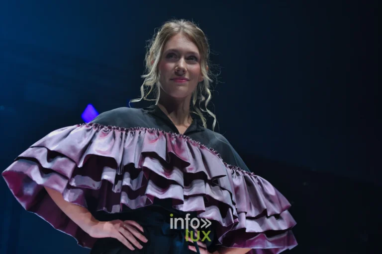 Cape en satin vieux rose à volants étagés, mains sur les hanches — Victoire Waxweiler, « Fragments », Lux Fashion Week 2026, Arlon