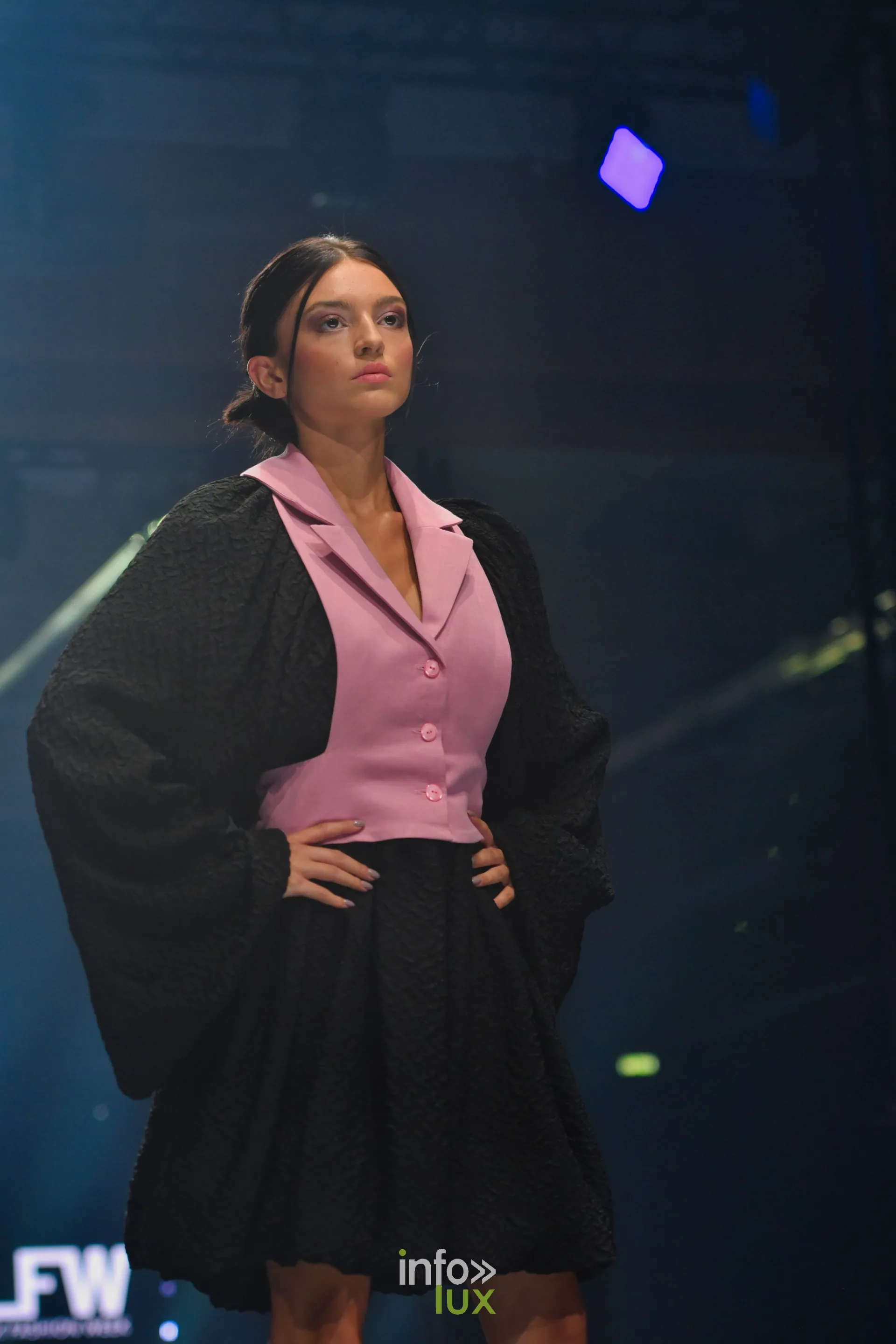 Gilet rose à revers sur veste-cape noire texturée et jupe boule noire — Victoire Waxweiler, « Fragments », Lux Fashion Week 2026, Arlon