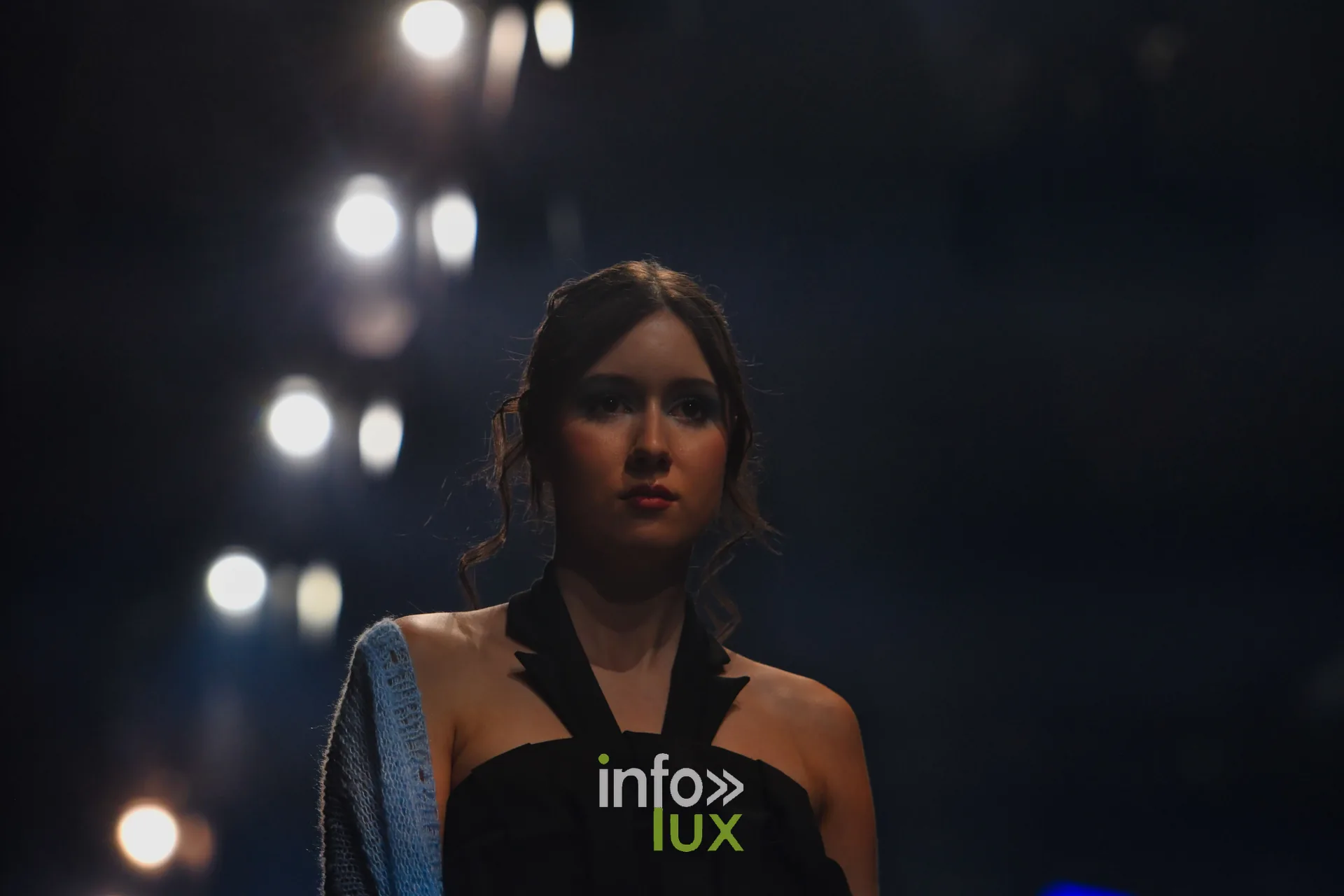 Haut noir à encolure licou, gilet en maille bleu clair sur l’épaule — Victoire Waxweiler, « Fragments », Lux Fashion Week 2026, Arlon