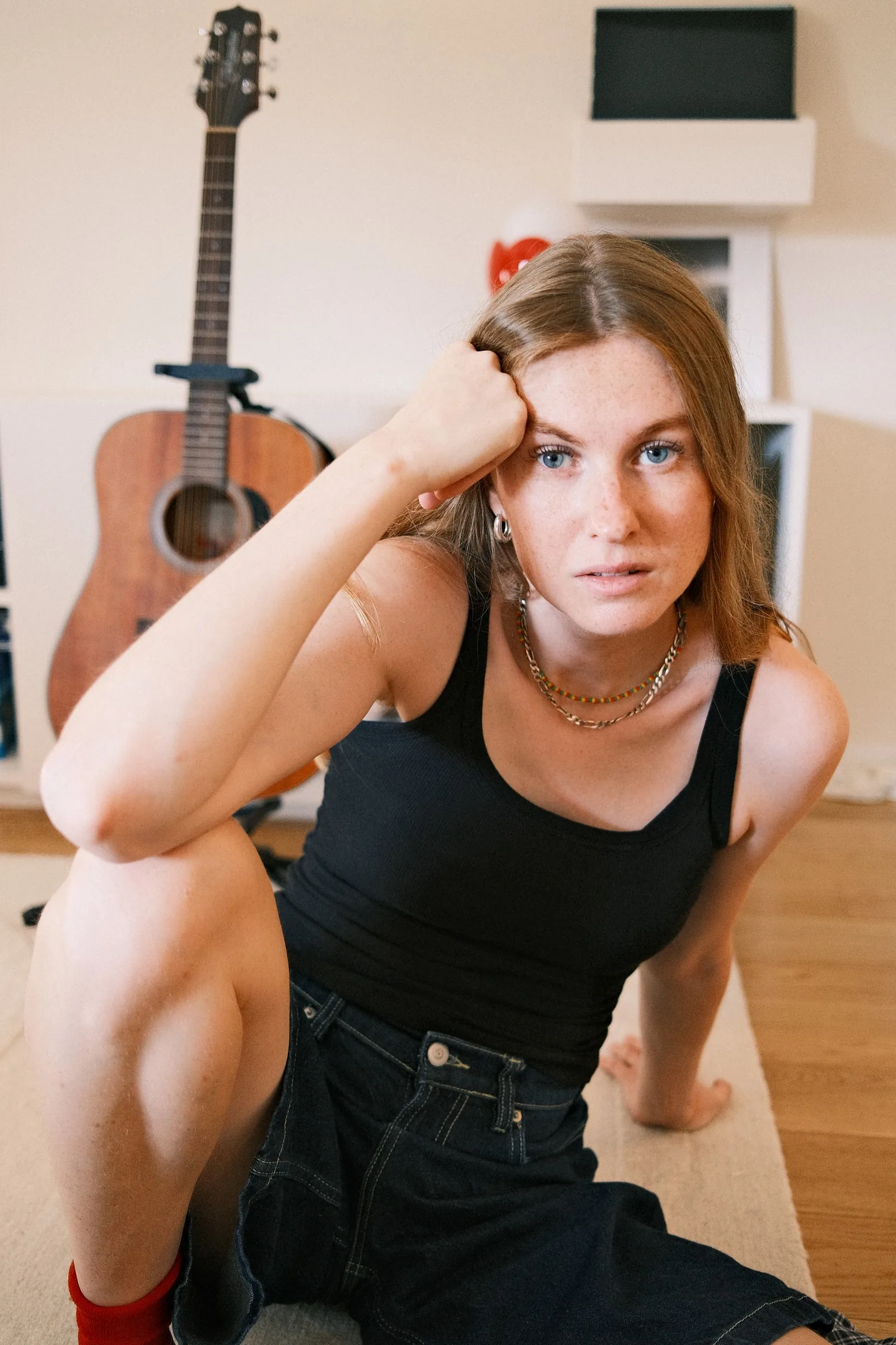 Maguie allongée, la main dans les cheveux, une guitare au mur
