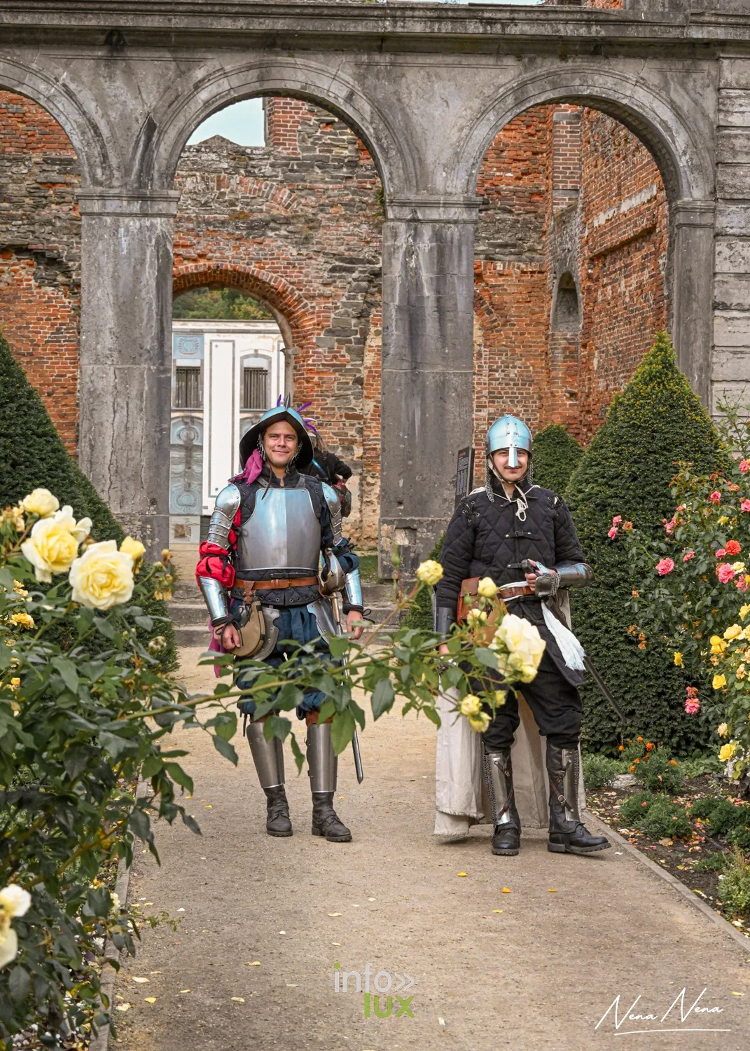 Deux chevaliers en armure marchent dans le jardin de roses de l’Abbaye de Villers, sous les arches en ruine