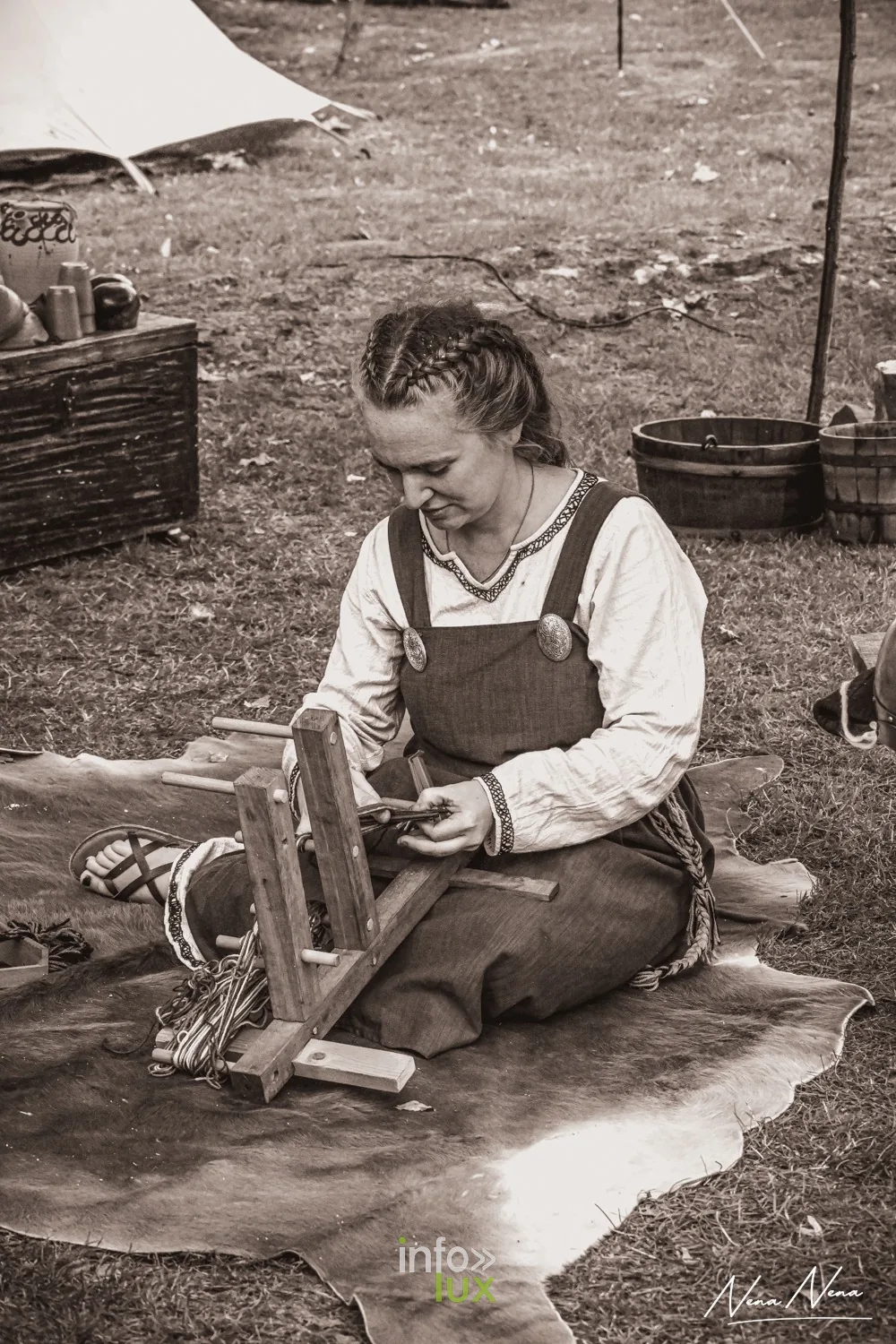 Une femme en robe médiévale tisse aux tablettes, assise sur une peau