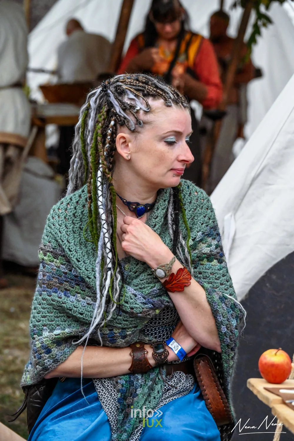 Portrait d’une femme aux longues tresses et châle vert, assise dans le campement