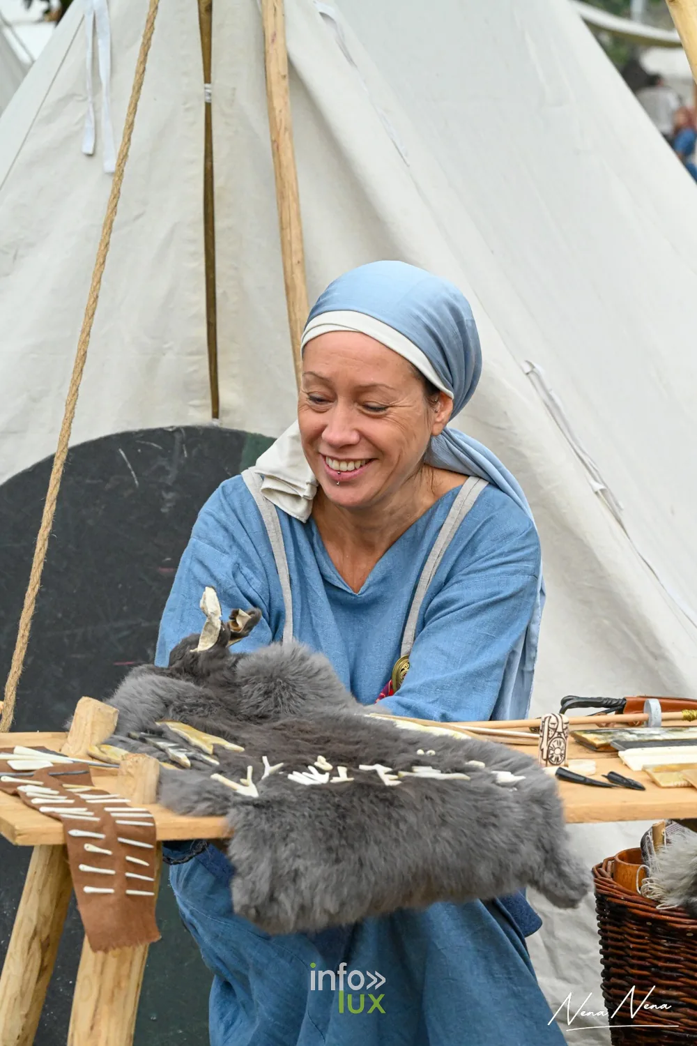Une femme en foulard bleu sourit derrière son étal d’os travaillés et de peaux
