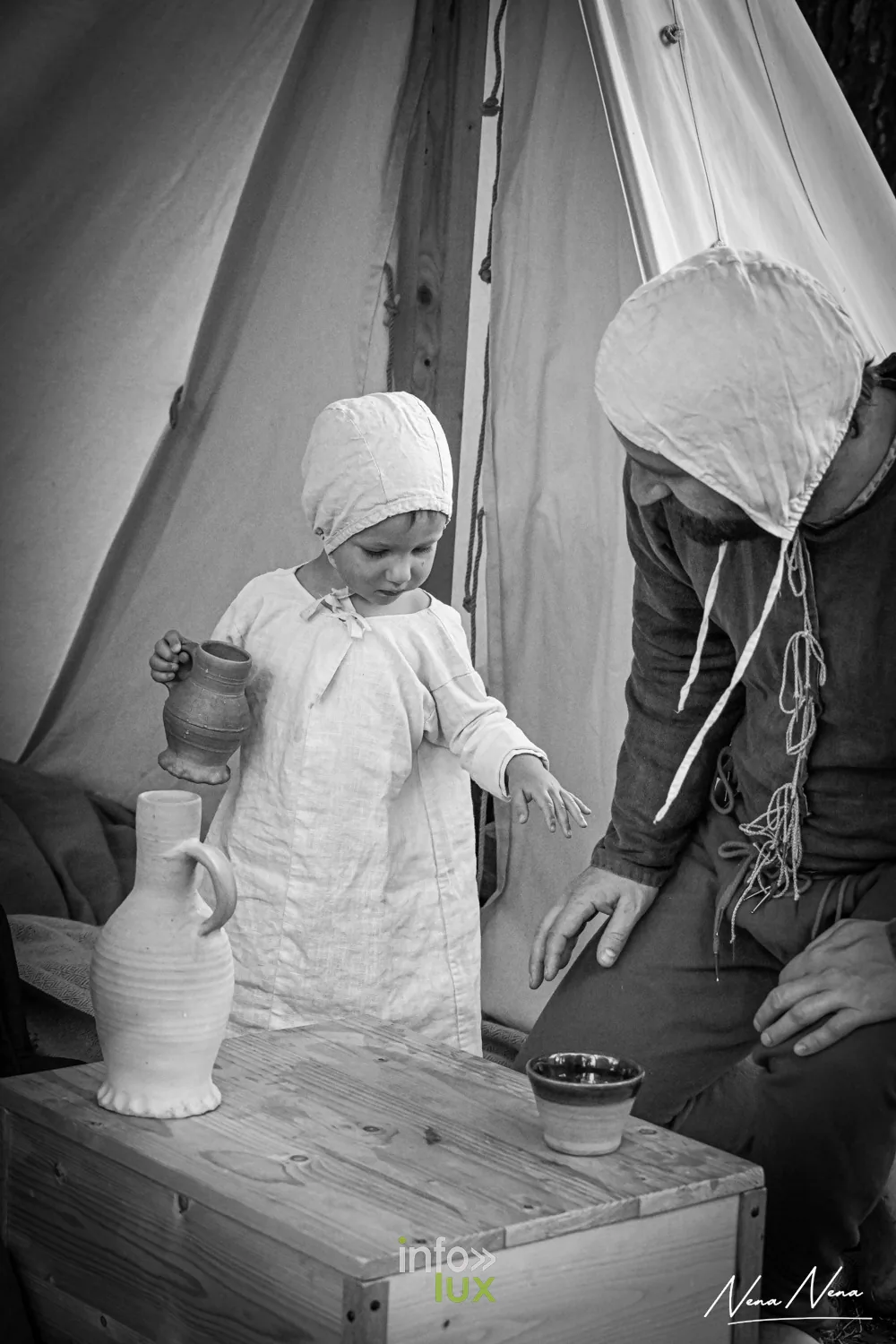 Un jeune enfant en chemise blanche tient une cruche sous une tente, en noir et blanc