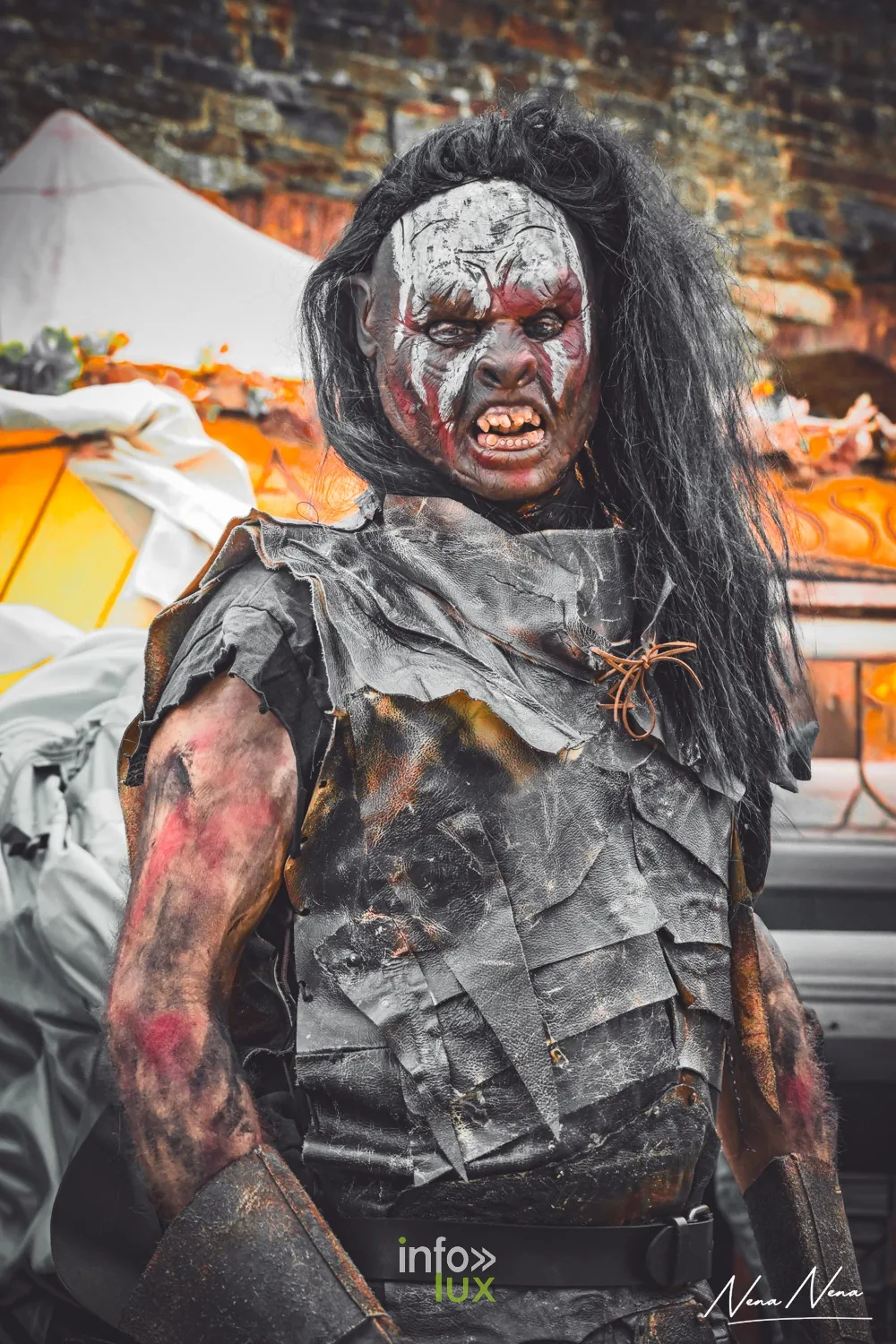 Un personnage grimé en orc, visage peint et dents postiches, devant les tentes
