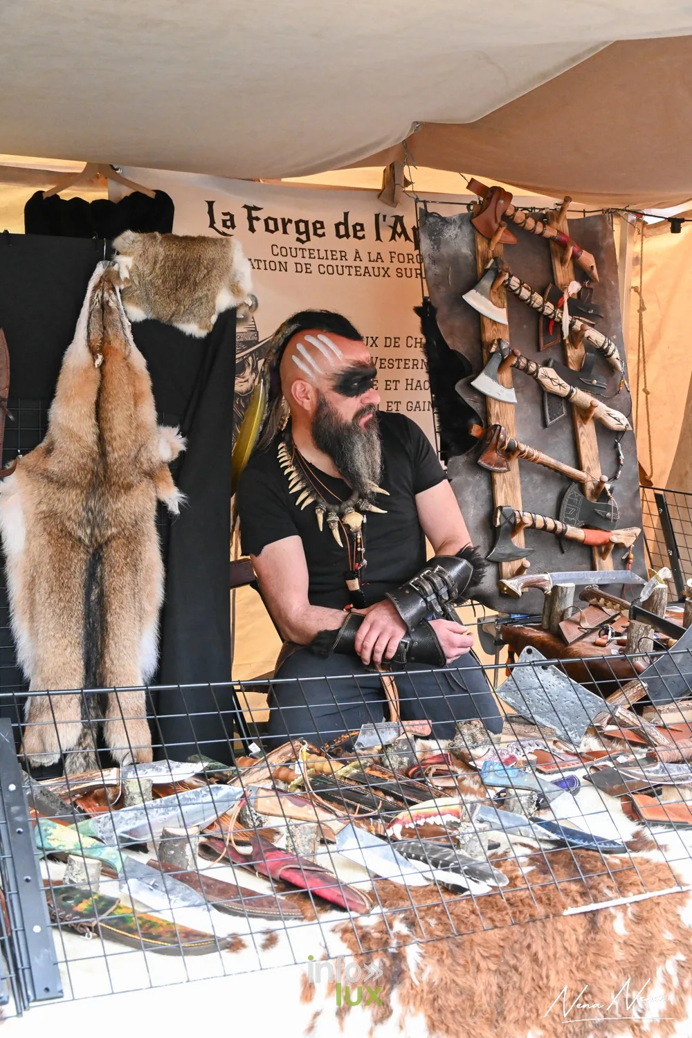 Le stand d’un coutelier-forgeron, peaux et couteaux exposés, l’artisan au visage peint derrière