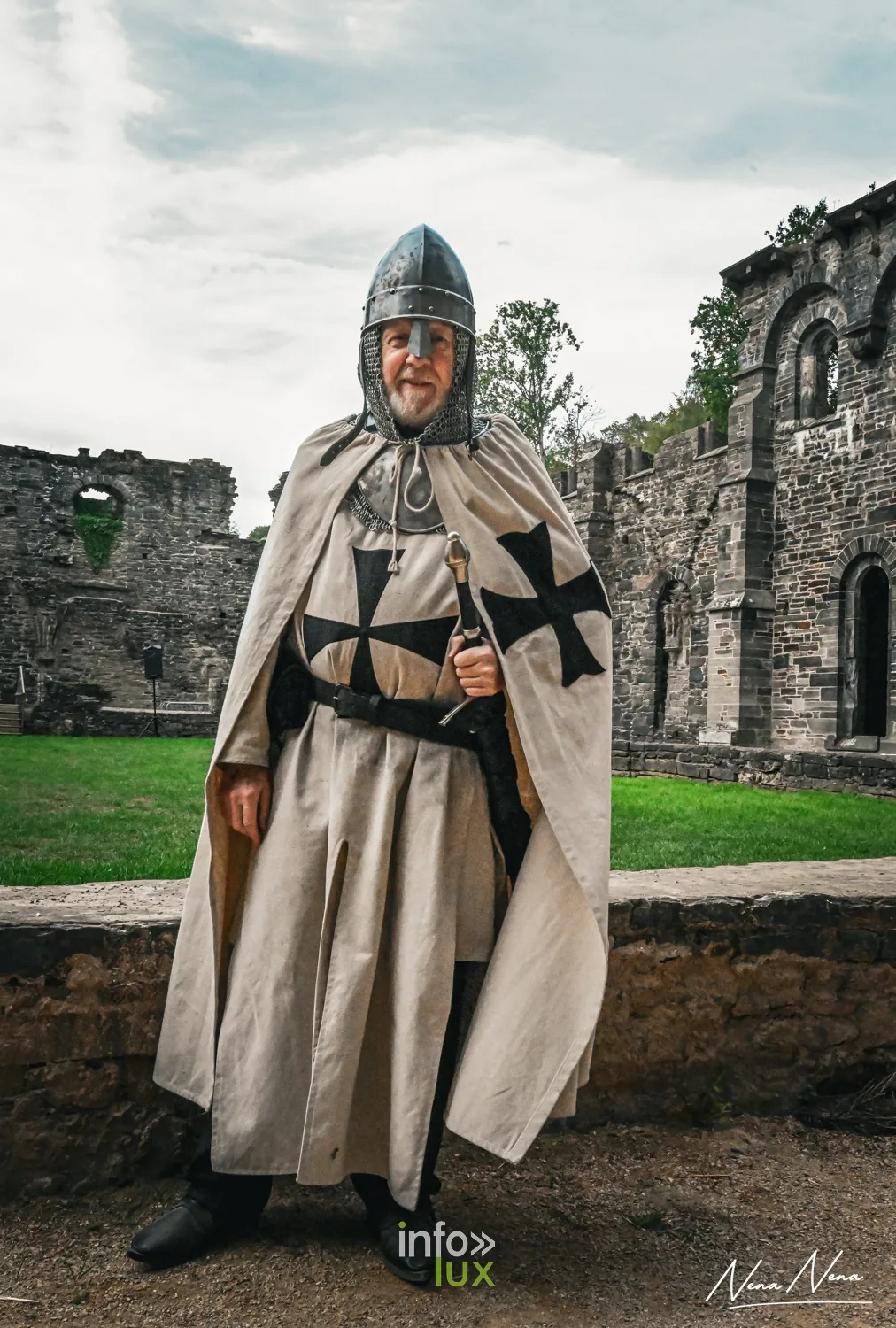 Un chevalier en cape blanche à croix noire pose devant les ruines de l’abbaye